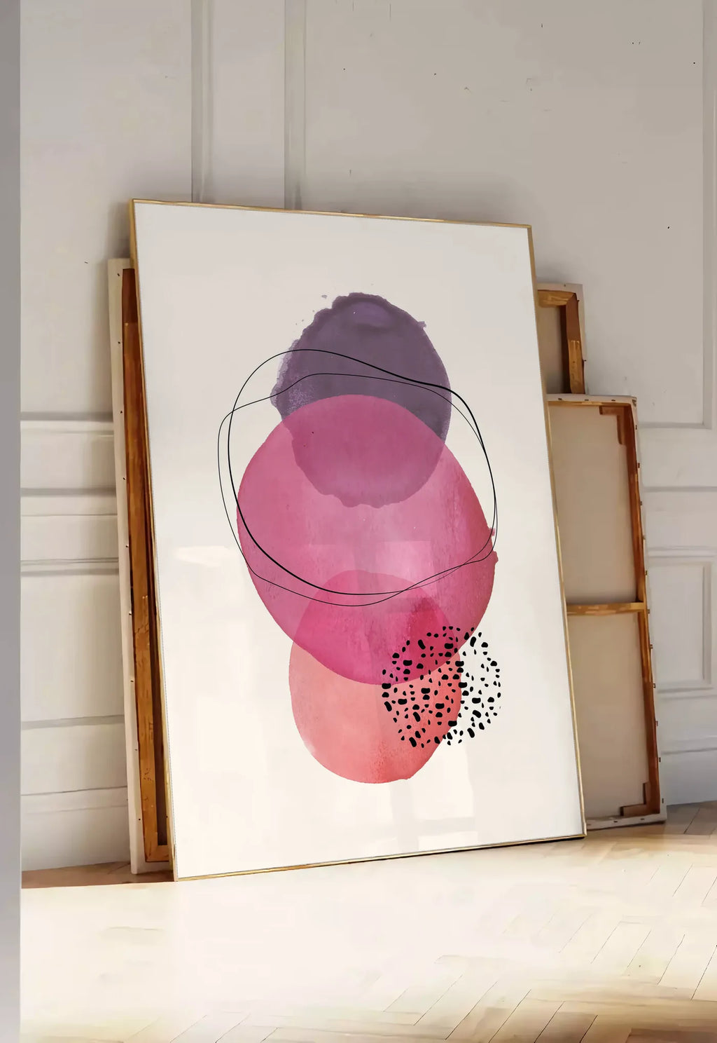 Tirage encadrable cercles aquarelle roses magenta et violets superposes sur creme, posee au sol dans une entree lumineuse, contre un mur a panneaux blancs, a cote de chassis en bois empiles