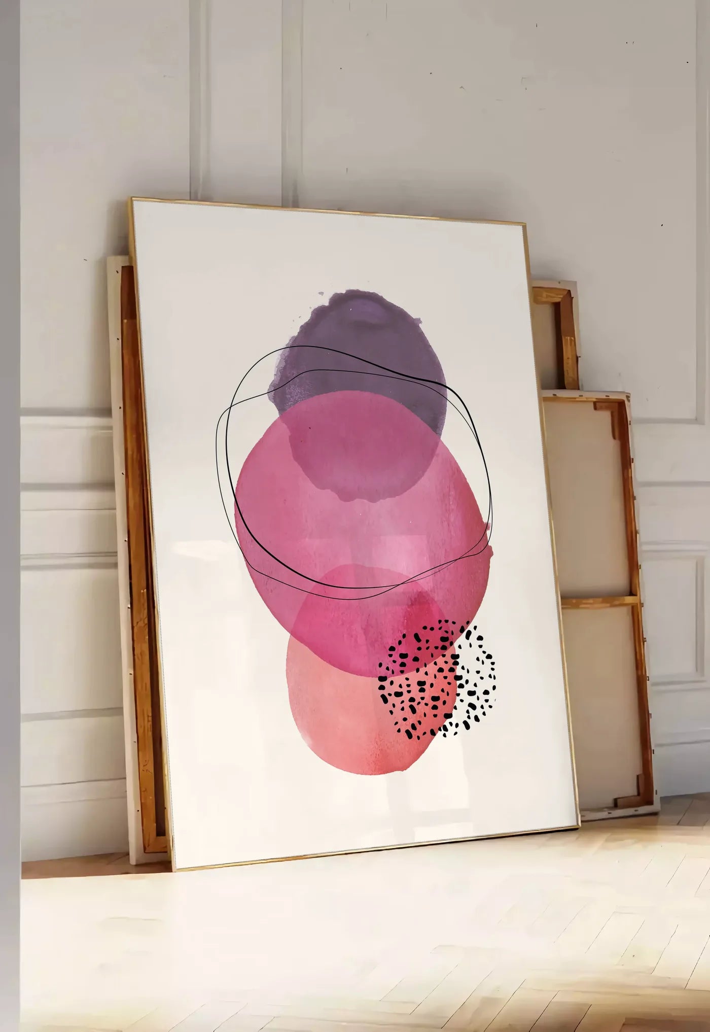 Tirage encadrable cercles aquarelle roses magenta et violets superposes sur creme, posee au sol dans une entree lumineuse, contre un mur a panneaux blancs, a cote de chassis en bois empiles