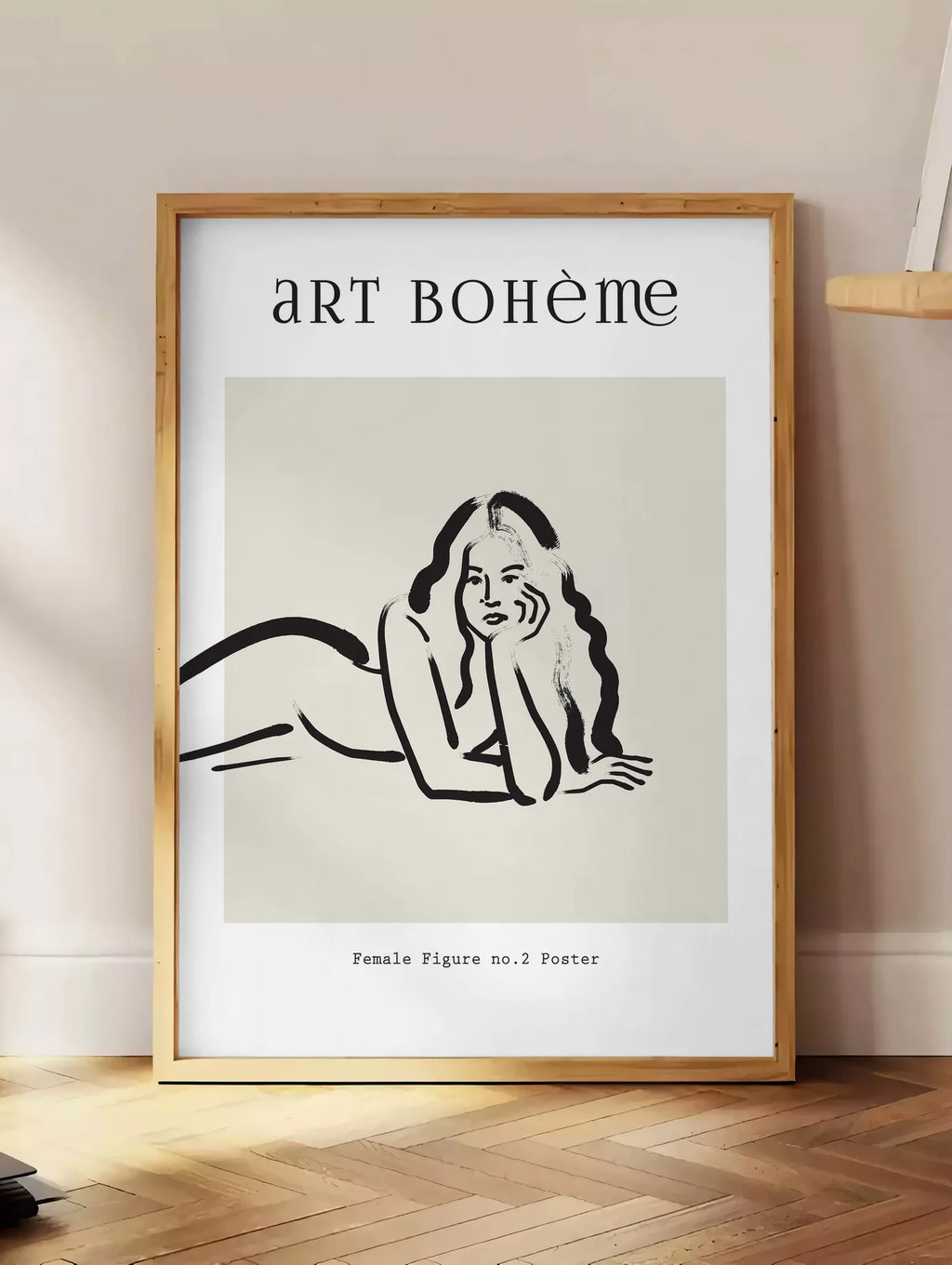 Estampe femme allongee au trait de pinceau noir sur creme, posee au sol dans un coin salon, sur un parquet a chevrons, pres d'une table d'appoint en chene chargee de livres