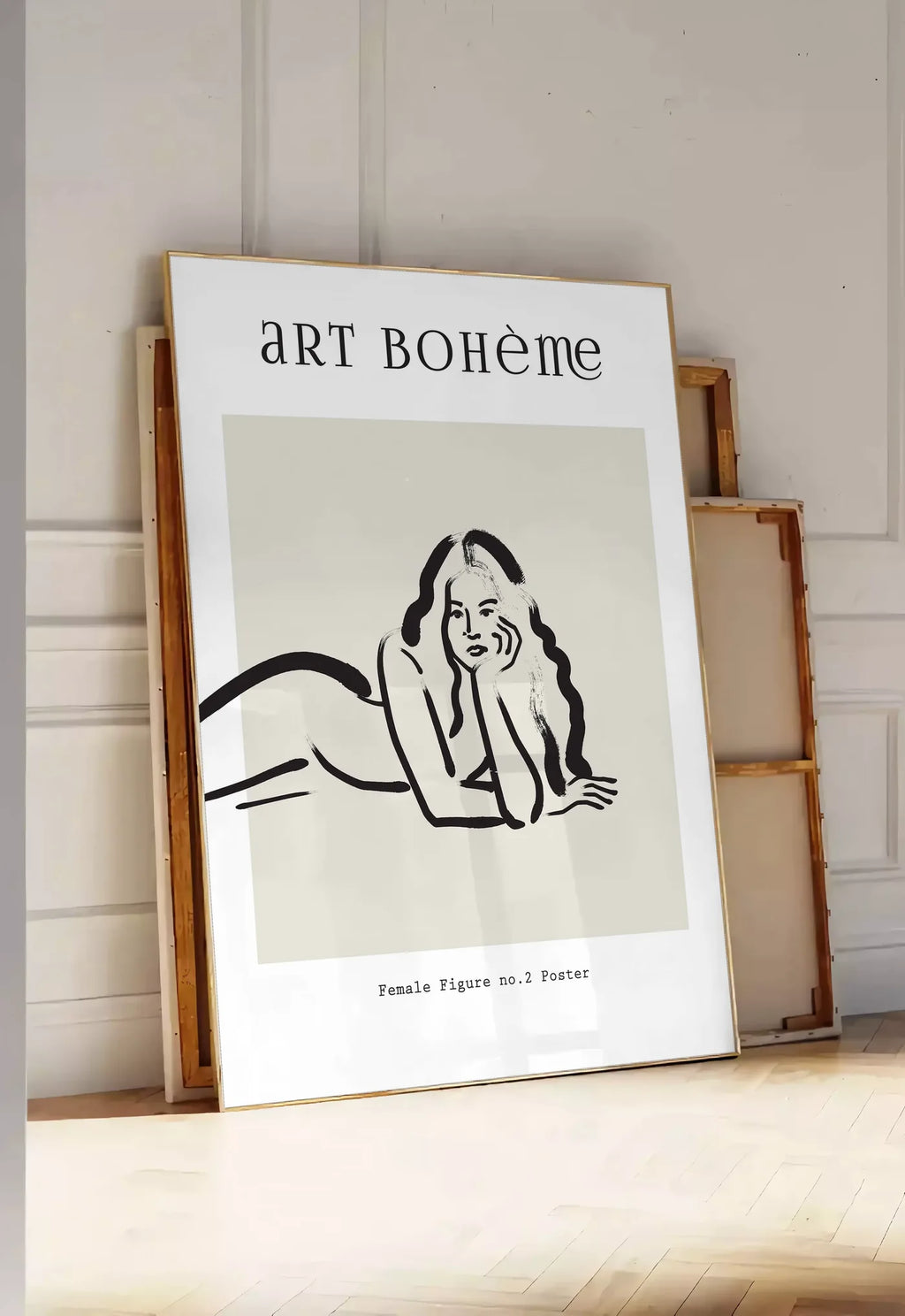 Tirage encadrable femme allongee au trait de pinceau noir sur creme, posee au sol dans une entree lumineuse, contre un mur a panneaux blancs, a cote de chassis en bois empiles