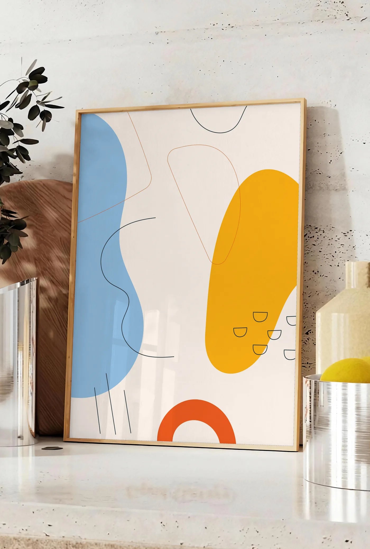 Affiche formes organiques bleu et jaune avec traits fins sur fond creme, posee sur un plan de travail de cuisine en pierre claire, entre une branche d'eucalyptus en vase et un bocal de citrons