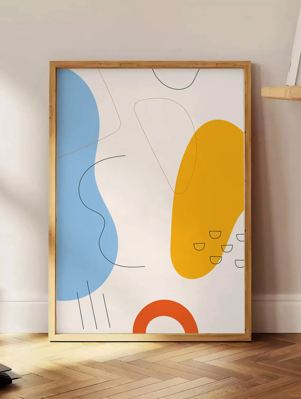 Estampe formes organiques bleu et jaune avec traits fins sur fond creme, posee au sol dans un coin salon, sur un parquet a chevrons, pres d'une table d'appoint en chene chargee de livres