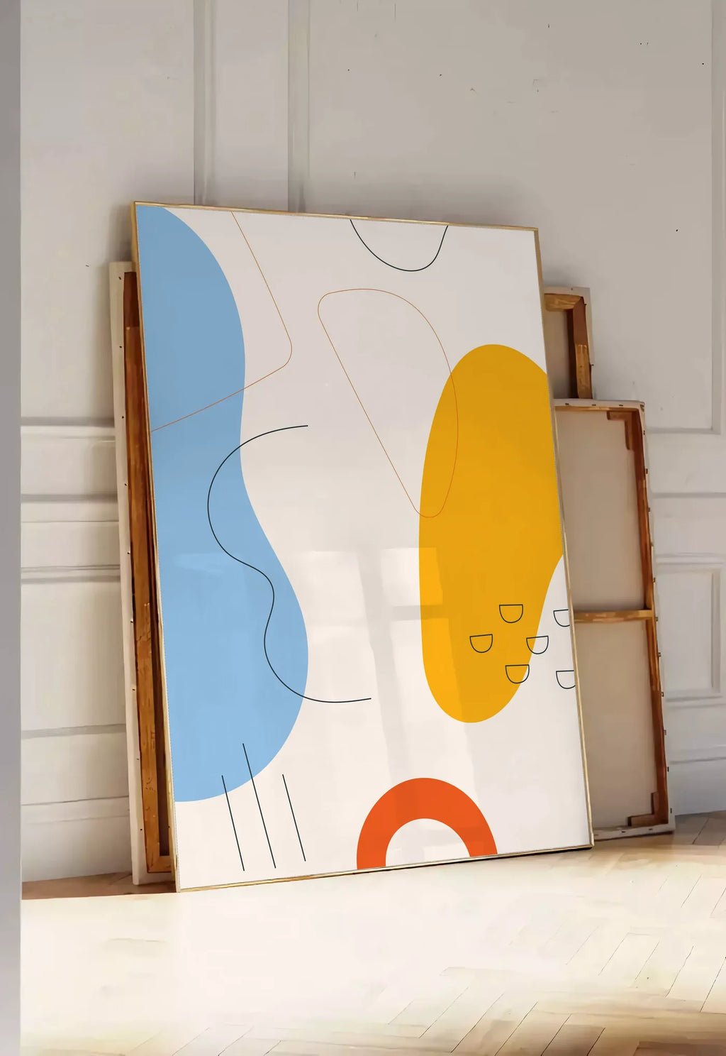 Tirage encadrable formes organiques bleu et jaune avec traits fins sur fond creme, posee au sol dans une entree lumineuse, contre un mur a panneaux blancs, a cote de chassis en bois empiles