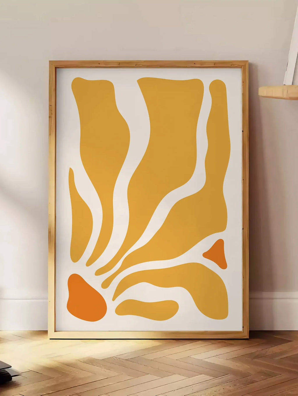Estampe formes organiques jaunes et orange ondulees sur fond creme, posee au sol dans un coin salon, sur un parquet a chevrons, pres d'une table d'appoint en chene chargee de livres