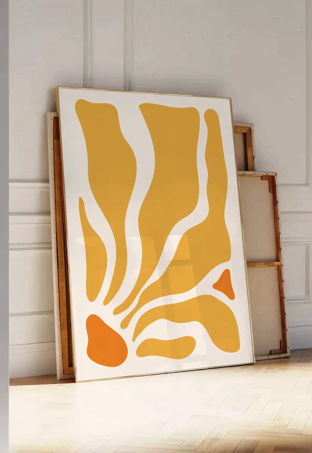 Tirage encadrable formes organiques jaunes et orange ondulees sur fond creme, posee au sol dans une entree lumineuse, contre un mur a panneaux blancs, a cote de chassis en bois empiles
