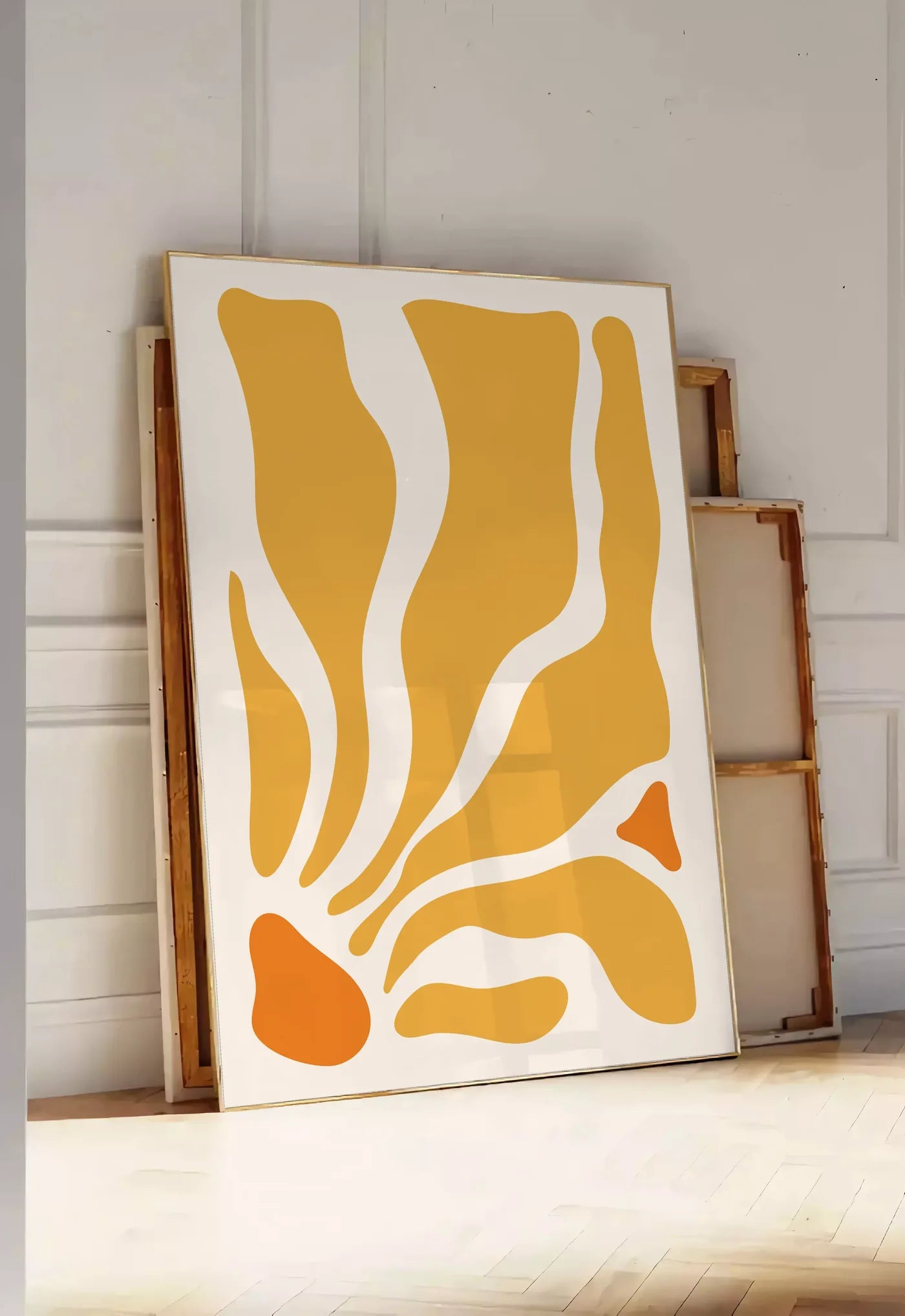 Tirage encadrable formes organiques jaunes et orange ondulees sur fond creme, posee au sol dans une entree lumineuse, contre un mur a panneaux blancs, a cote de chassis en bois empiles
