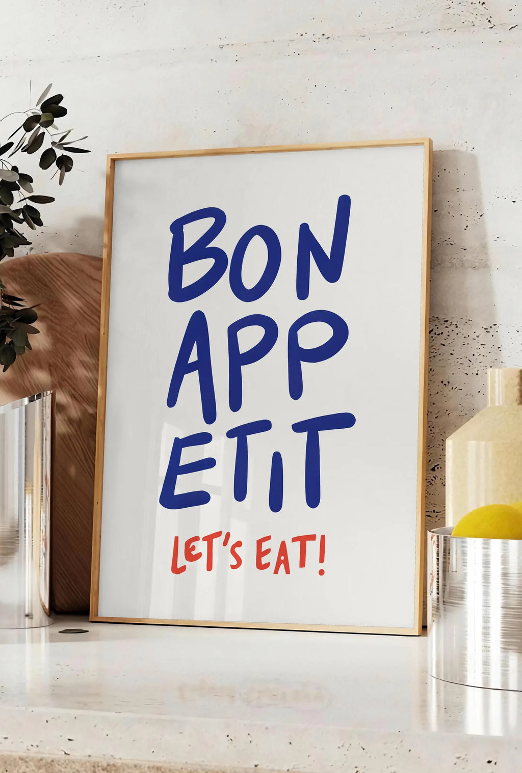Affiche affiche cuisine Bon Appetit, posee sur un plan de travail de cuisine en pierre claire, entre une branche d'eucalyptus en vase et un bocal de citrons