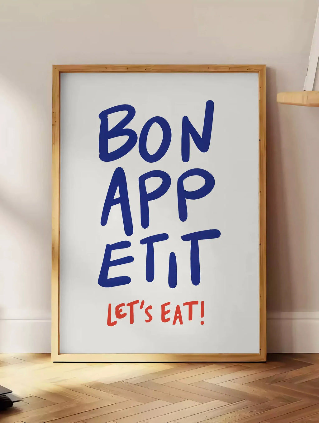 Estampe affiche cuisine Bon Appetit, posee au sol dans un coin salon, sur un parquet a chevrons, pres d'une table d'appoint en chene chargee de livres