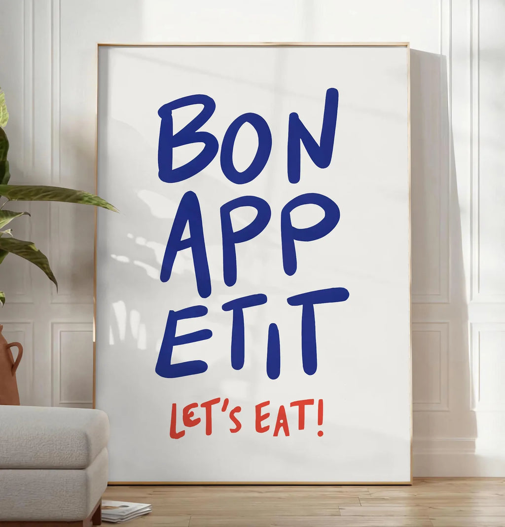 Reproduction affiche cuisine Bon Appetit, posee au sol dans un salon minimaliste clair, a cote d'un canape beige et d'une plante verte, sur un parquet clair