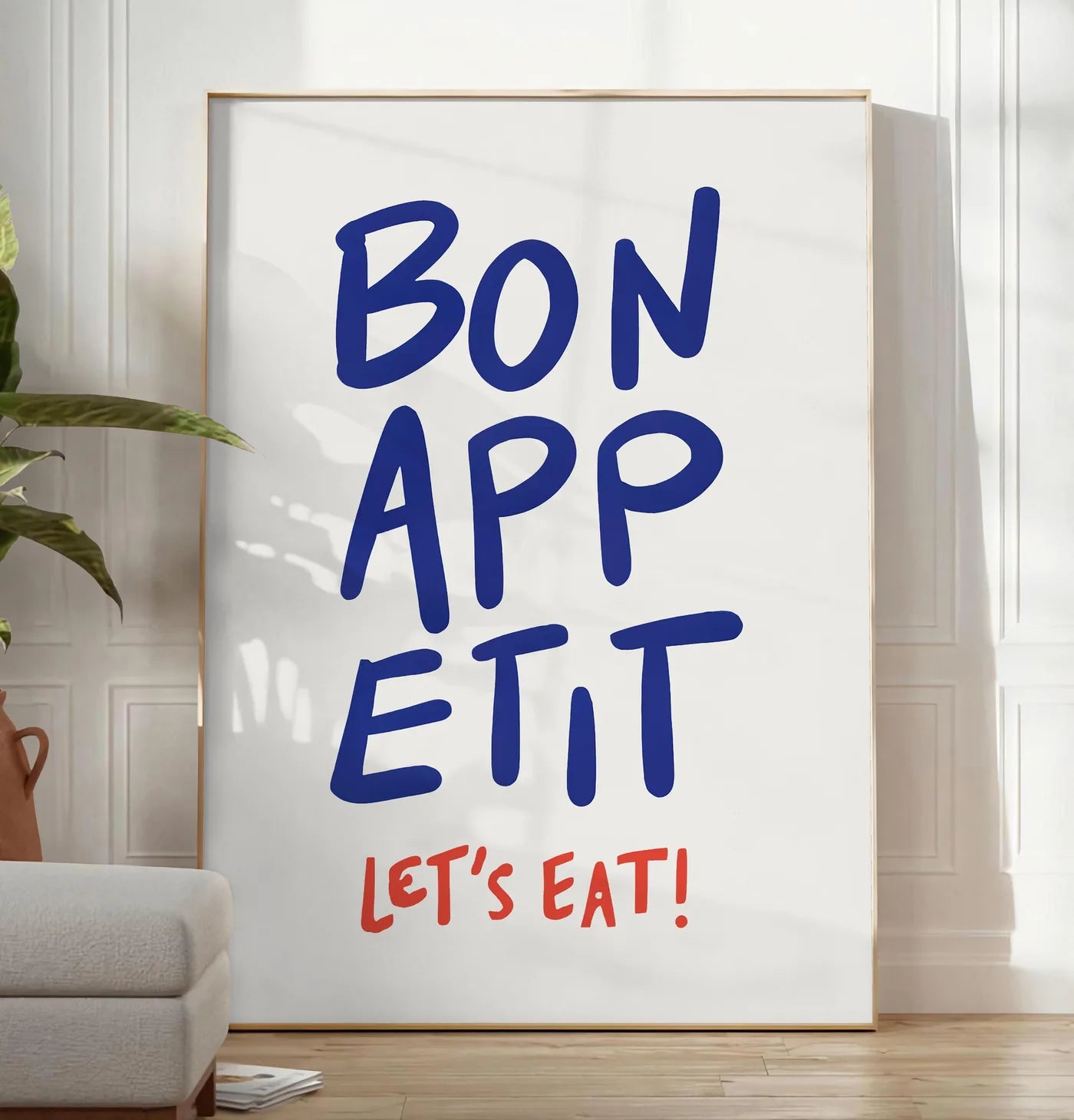 Reproduction affiche cuisine Bon Appetit, posee au sol dans un salon minimaliste clair, a cote d'un canape beige et d'une plante verte, sur un parquet clair