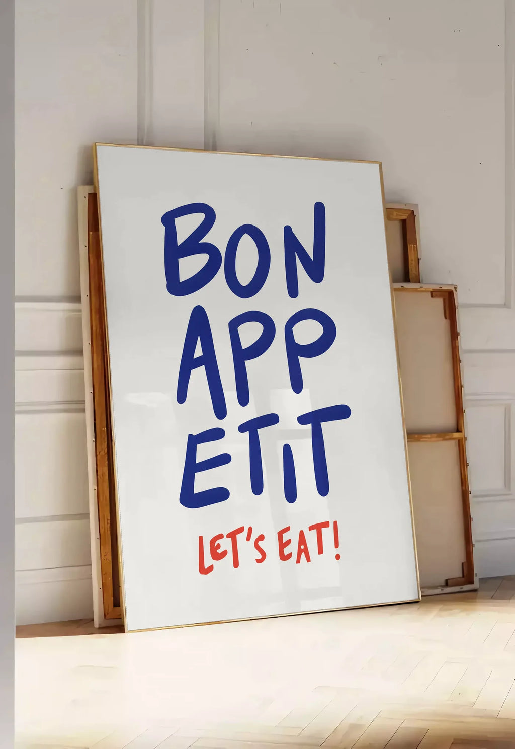 Tirage encadrable affiche cuisine Bon Appetit, posee au sol dans une entree lumineuse, contre un mur a panneaux blancs, a cote de chassis en bois empiles