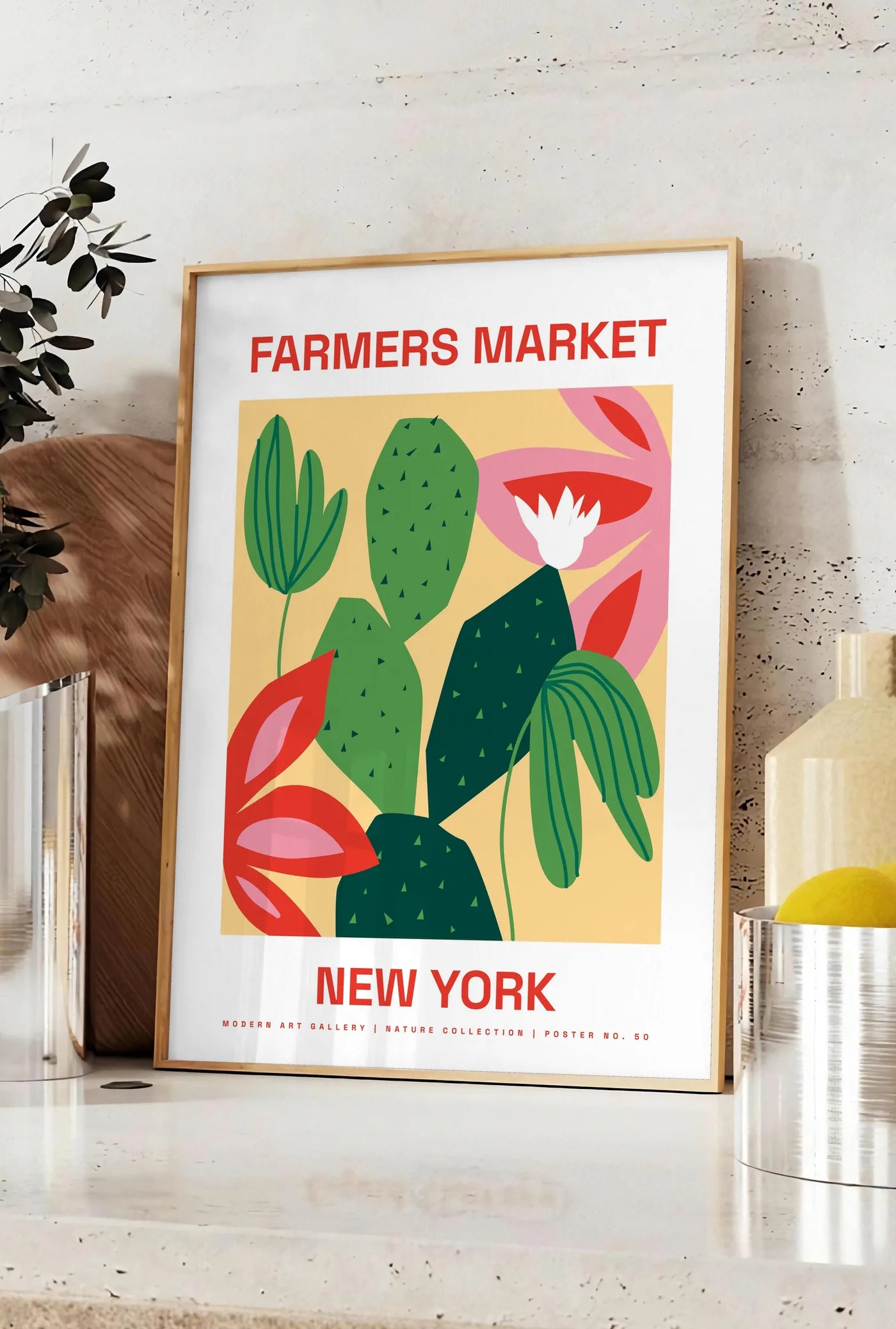 Affiche affiche botanique cactus et feuilles rayees, posee sur un plan de travail de cuisine en pierre claire, entre une branche d'eucalyptus en vase et un bocal de citrons