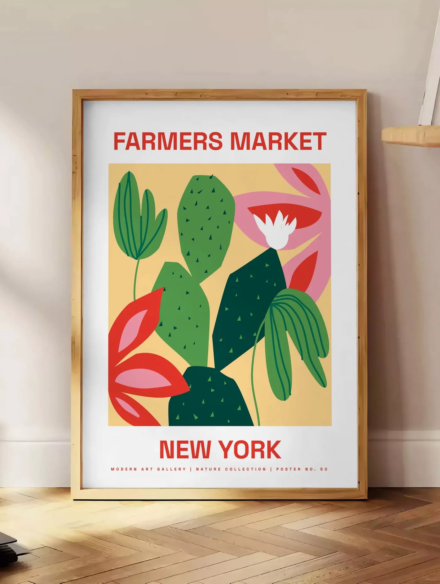 Estampe affiche botanique cactus et feuilles rayees, posee au sol dans un coin salon, sur un parquet a chevrons, pres d'une table d'appoint en chene chargee de livres