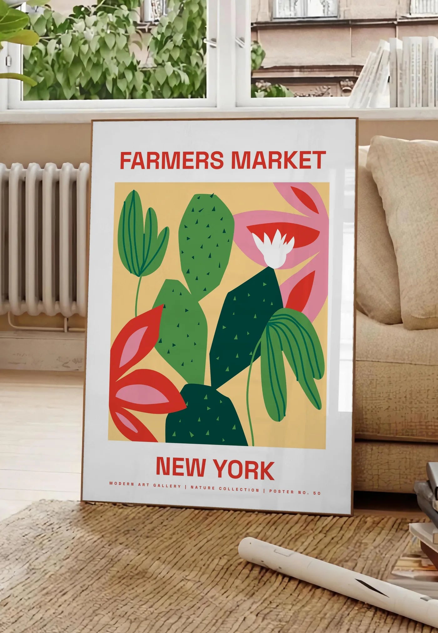 Poster affiche botanique cactus et feuilles rayees, posee au sol dans un salon parisien, devant une grande fenetre donnant sur un immeuble haussmannien, entre un ficus et un canape creme