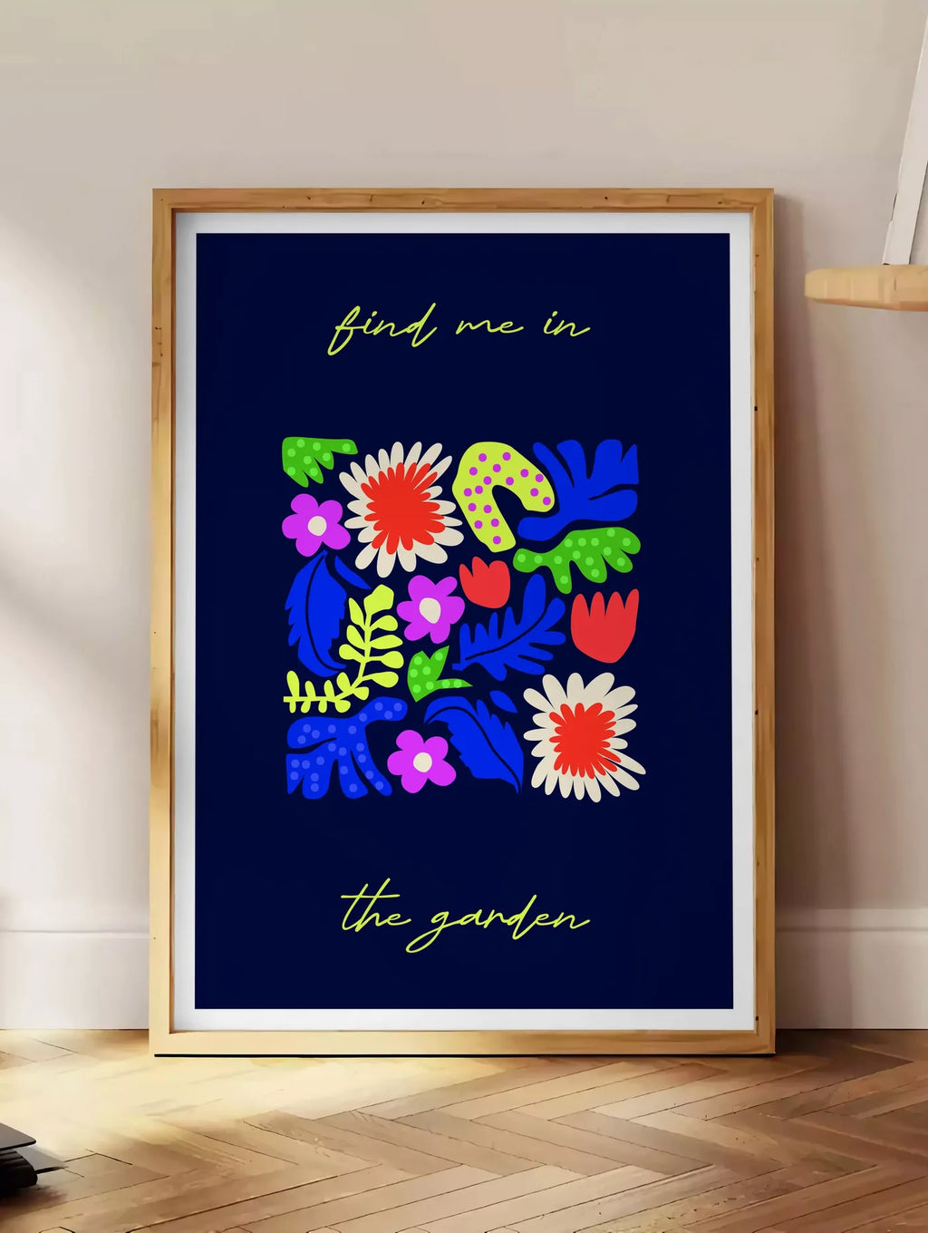 Estampe affiche botanique fleurs folk, posee au sol dans un coin salon, sur un parquet a chevrons, pres d'une table d'appoint en chene chargee de livres