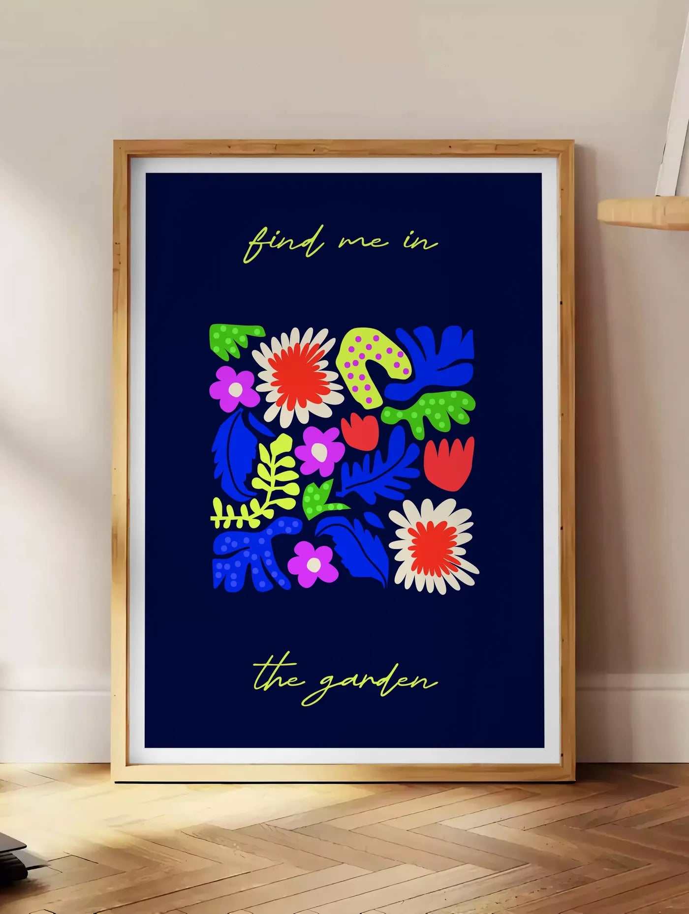 Estampe affiche botanique fleurs folk, posee au sol dans un coin salon, sur un parquet a chevrons, pres d'une table d'appoint en chene chargee de livres