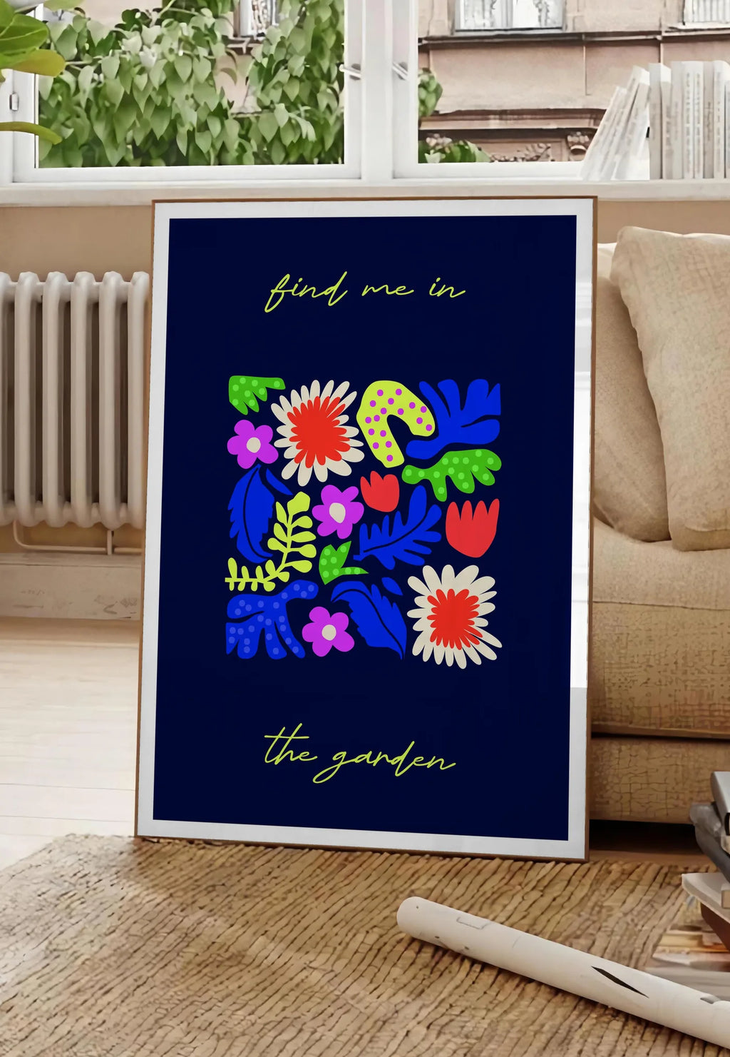 Poster affiche botanique fleurs folk, posee au sol dans un salon parisien, devant une grande fenetre donnant sur un immeuble haussmannien, entre un ficus et un canape creme