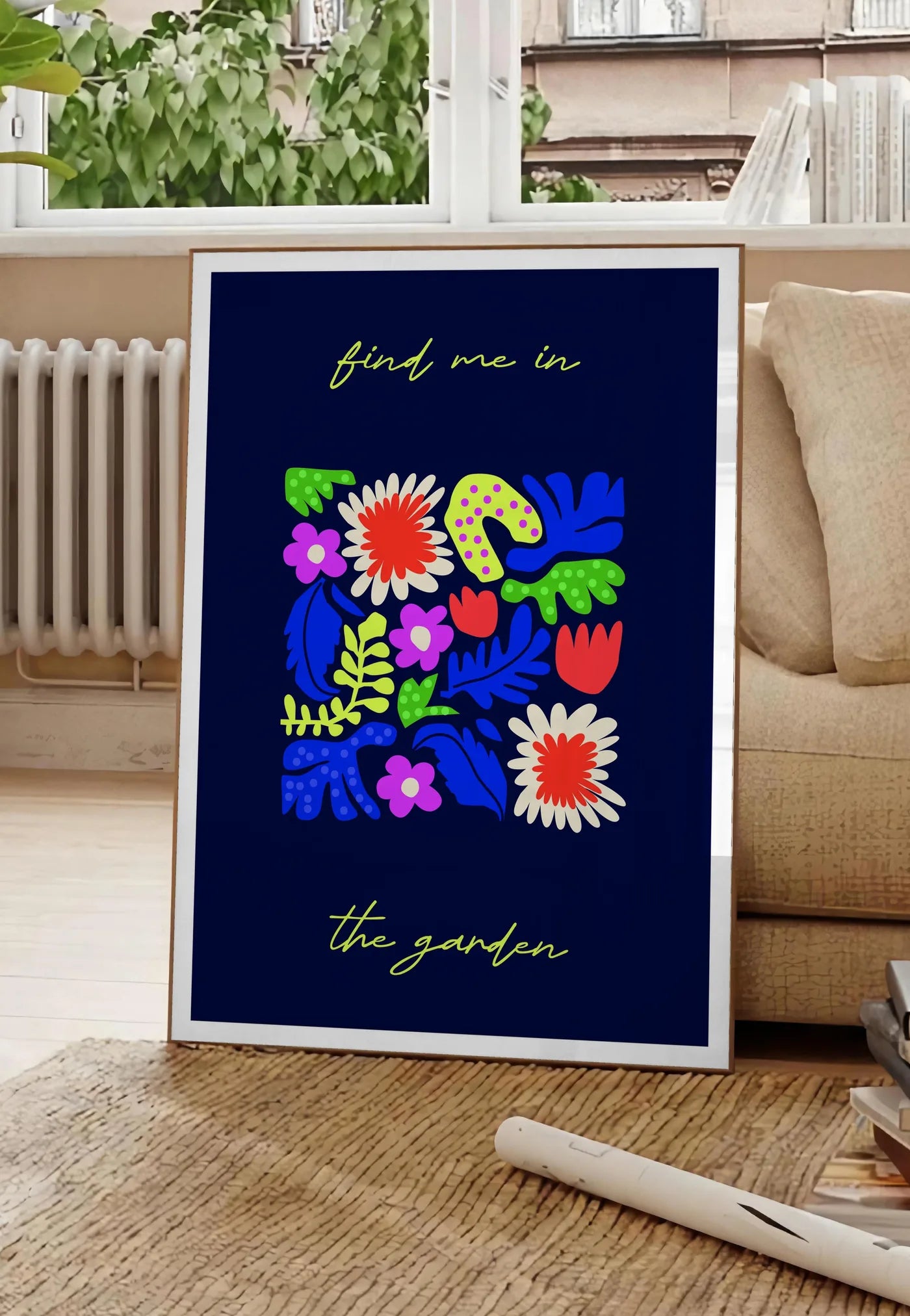 Poster affiche botanique fleurs folk, posee au sol dans un salon parisien, devant une grande fenetre donnant sur un immeuble haussmannien, entre un ficus et un canape creme