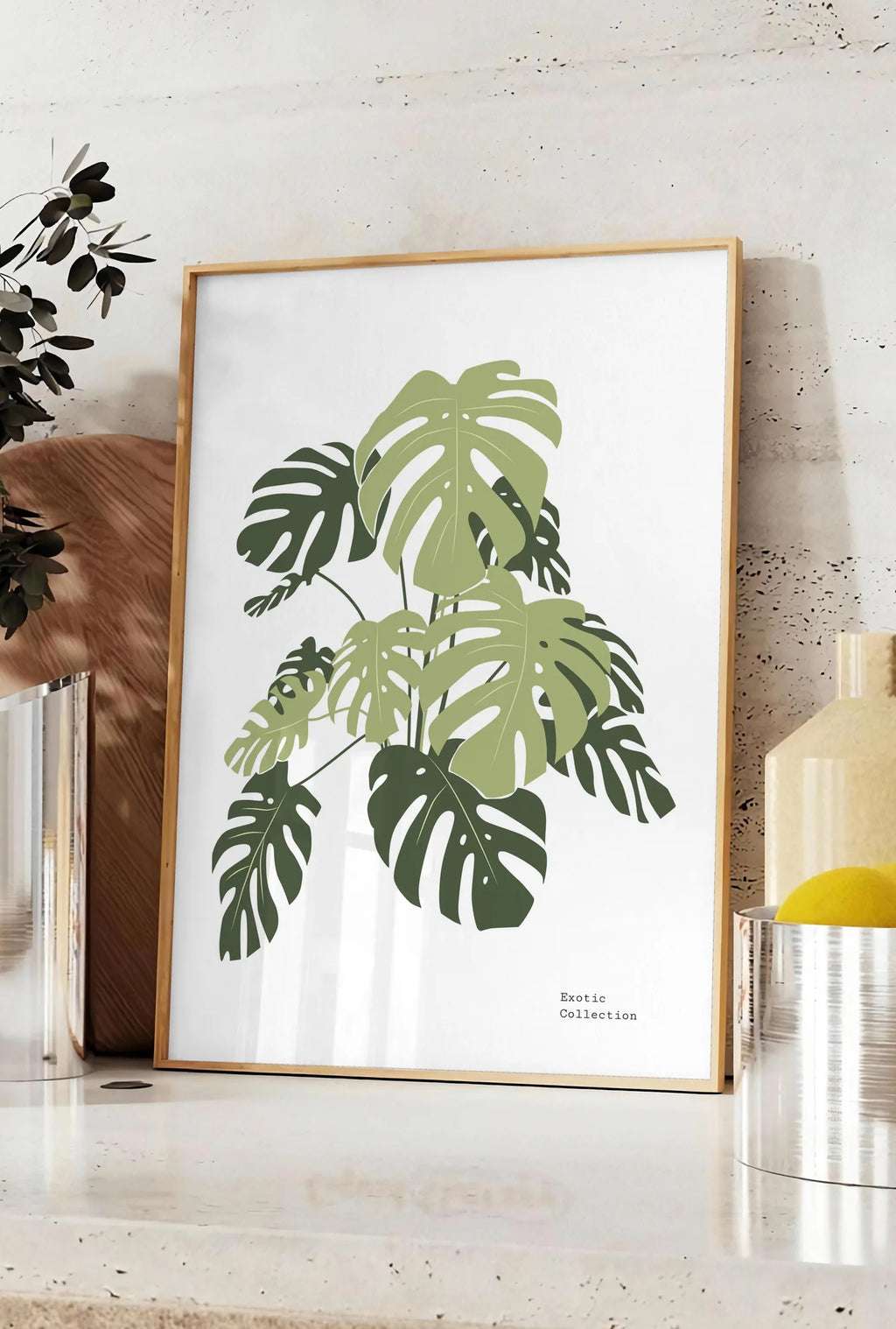Affiche affiche monstera botanique, posee sur un plan de travail de cuisine en pierre claire, entre une branche d'eucalyptus en vase et un bocal de citrons