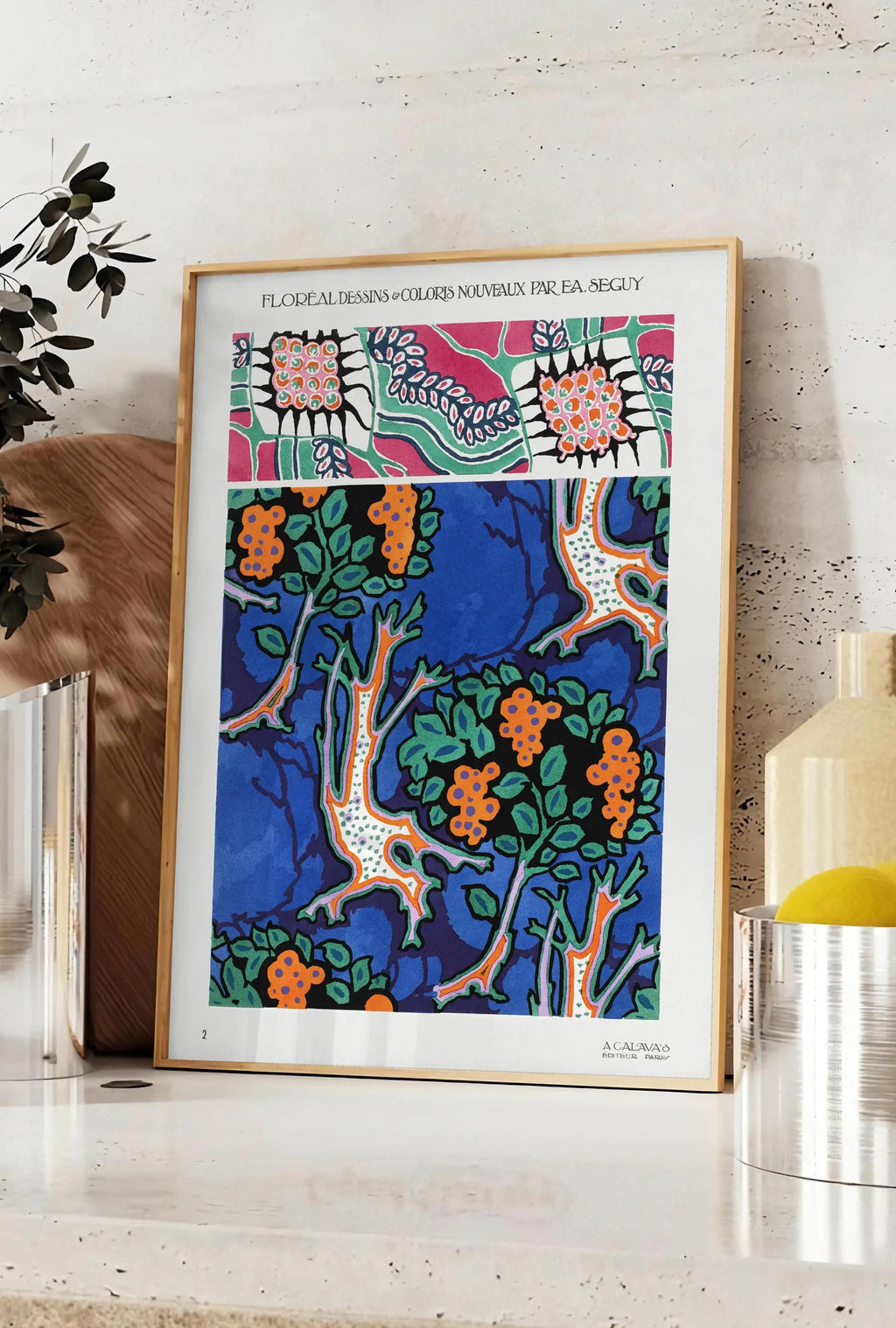 Affiche planches botaniques montrent des grappes de fruits stylisées sur fond bleu de cobalt, posee sur un plan de travail de cuisine en pierre claire, entre une branche d'eucalyptus en vase et un bocal de citrons
