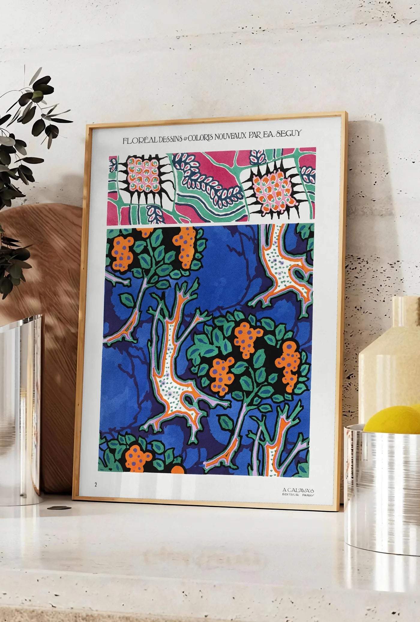 Affiche planches botaniques montrent des grappes de fruits stylisées sur fond bleu de cobalt, posee sur un plan de travail de cuisine en pierre claire, entre une branche d'eucalyptus en vase et un bocal de citrons