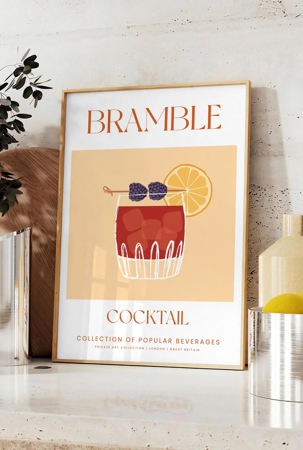 Affiche affiche cocktail Bramble, posee sur un plan de travail de cuisine en pierre claire, entre une branche d'eucalyptus en vase et un bocal de citrons