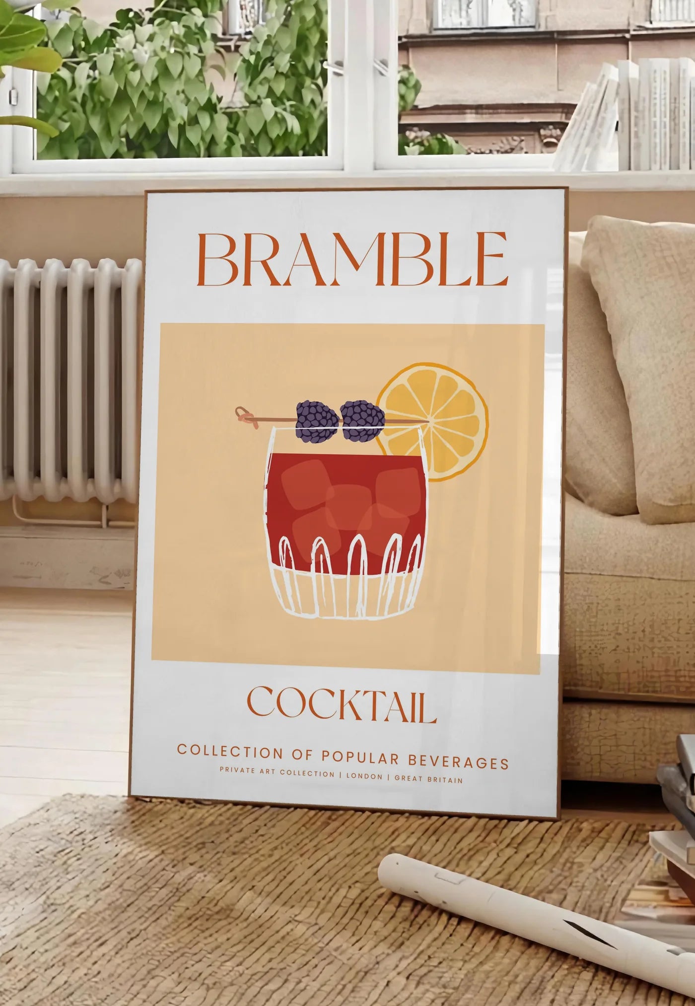 Poster affiche cocktail Bramble, posee au sol dans un salon parisien, devant une grande fenetre donnant sur un immeuble haussmannien, entre un ficus et un canape creme