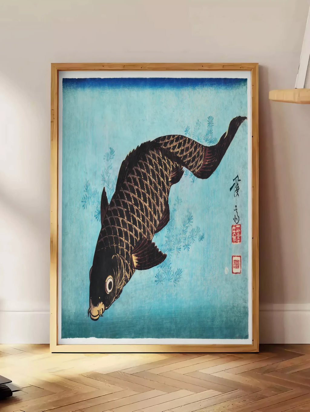 Estampe affiche carpe noire sur fond bleu art japonais, posee au sol dans un coin salon, sur un parquet a chevrons, pres d'une table d'appoint en chene chargee de livres