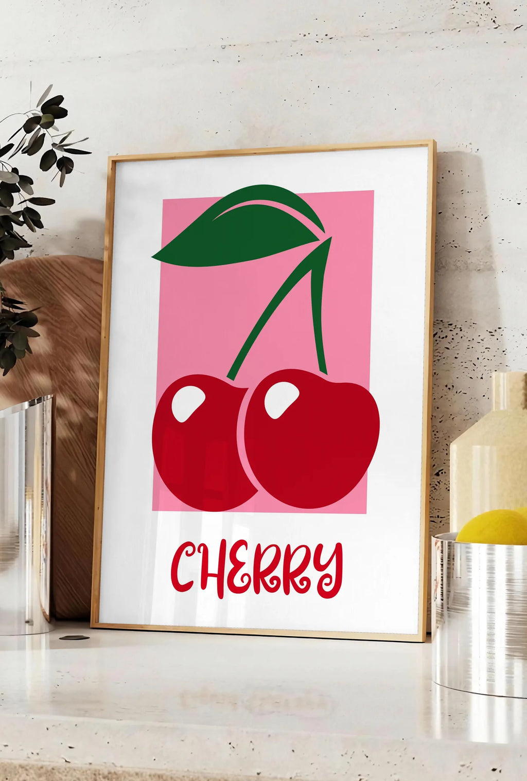 Affiche affiche cuisine cerises cherry fruit rouges et feuille verte sur panneau rose, posee sur un plan de travail de cuisine en pierre claire, entre une branche d'eucalyptus en vase et un bocal de citrons