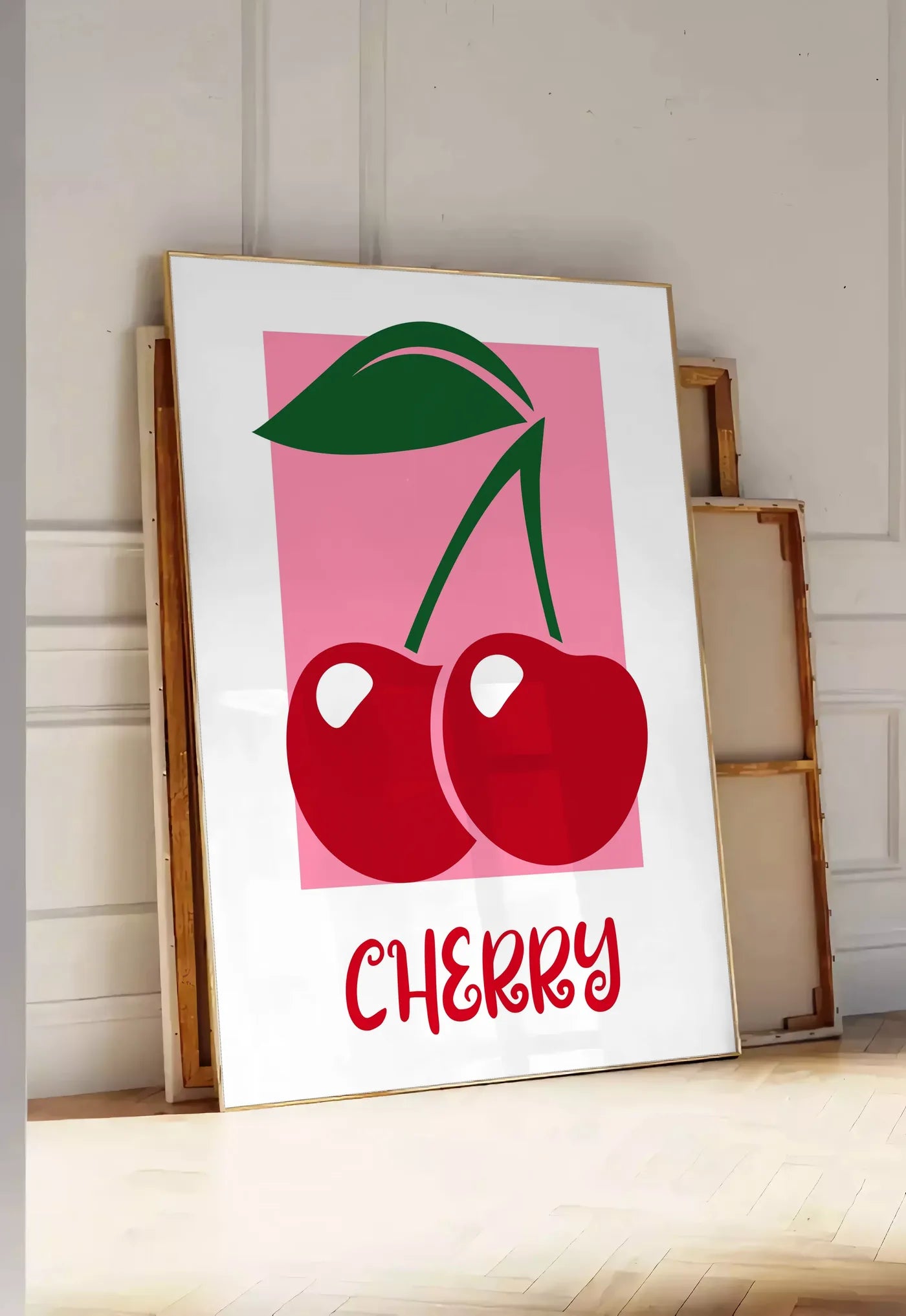 Tirage encadrable affiche cuisine cerises cherry fruit rouges et feuille verte sur panneau rose, posee au sol dans une entree lumineuse, contre un mur a panneaux blancs, a cote de chassis en bois empiles