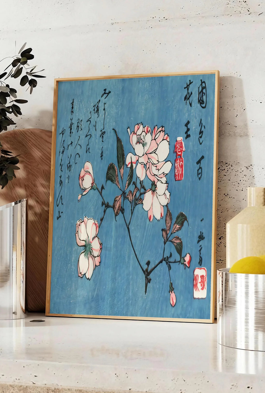 Affiche affiche cerisier en fleurs sur fond bleu art japonais, posee sur un plan de travail de cuisine en pierre claire, entre une branche d'eucalyptus en vase et un bocal de citrons
