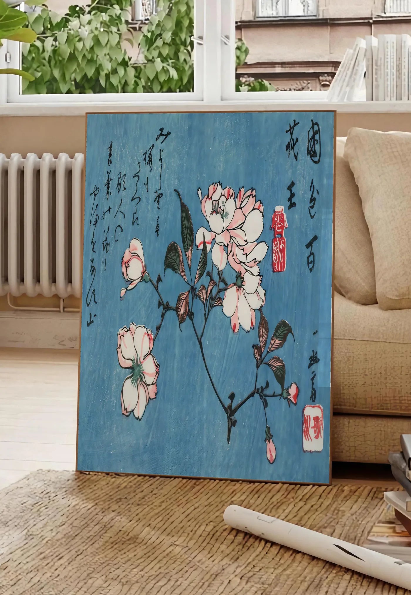 Poster affiche cerisier en fleurs sur fond bleu art japonais, posee au sol dans un salon parisien, devant une grande fenetre donnant sur un immeuble haussmannien, entre un ficus et un canape creme