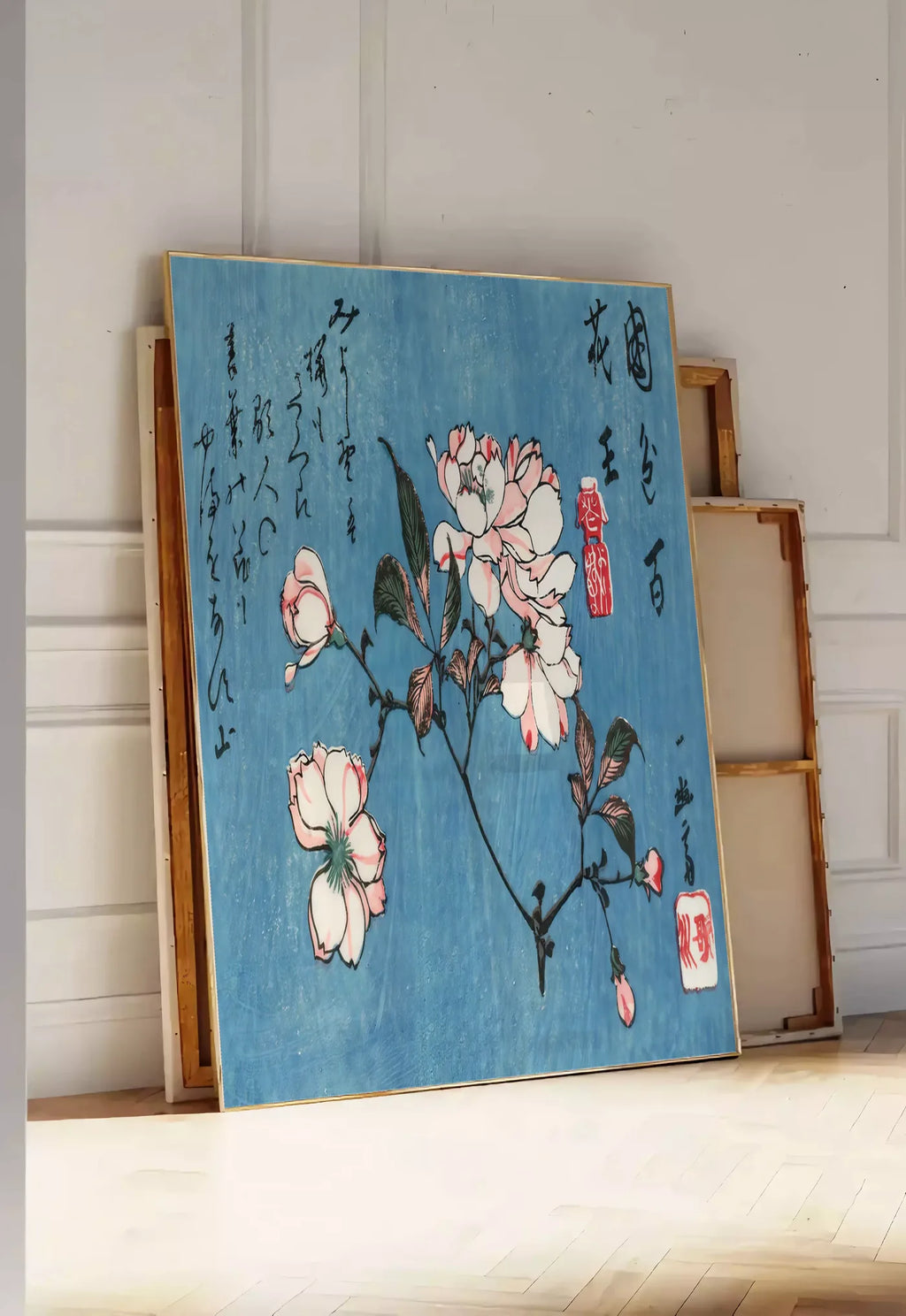 Tirage encadrable affiche cerisier en fleurs sur fond bleu art japonais, posee au sol dans une entree lumineuse, contre un mur a panneaux blancs, a cote de chassis en bois empiles