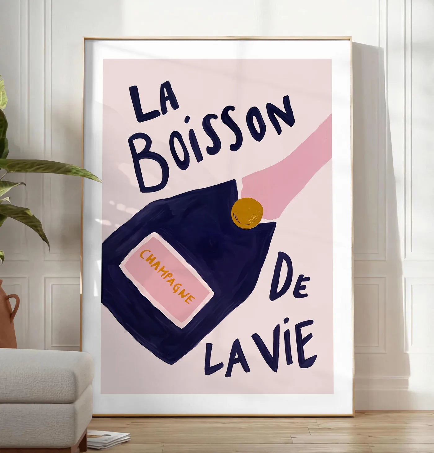 Reproduction affiche champagne La Boisson de la Vie, posee au sol dans un salon minimaliste clair, a cote d'un canape beige et d'une plante verte, sur un parquet clair