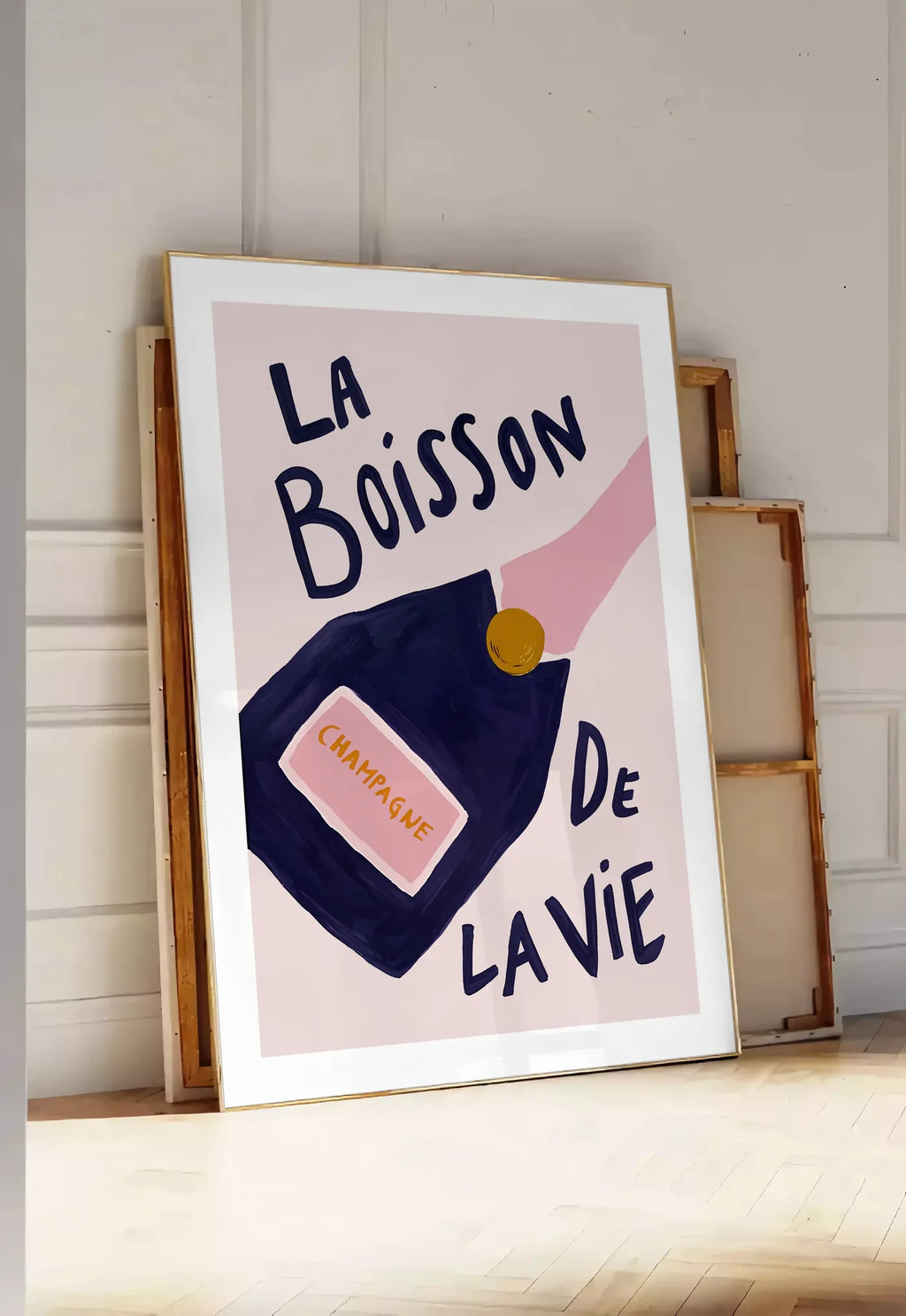 Tirage encadrable affiche champagne La Boisson de la Vie, posee au sol dans une entree lumineuse, contre un mur a panneaux blancs, a cote de chassis en bois empiles