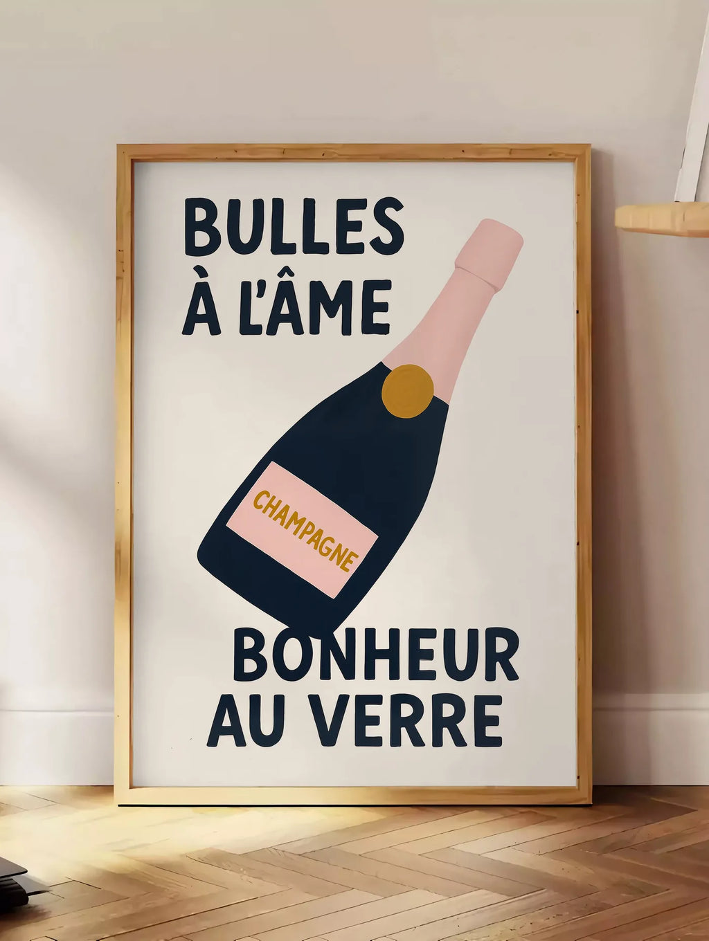 Estampe affiche champagne Bulles a l'ame, posee au sol dans un coin salon, sur un parquet a chevrons, pres d'une table d'appoint en chene chargee de livres