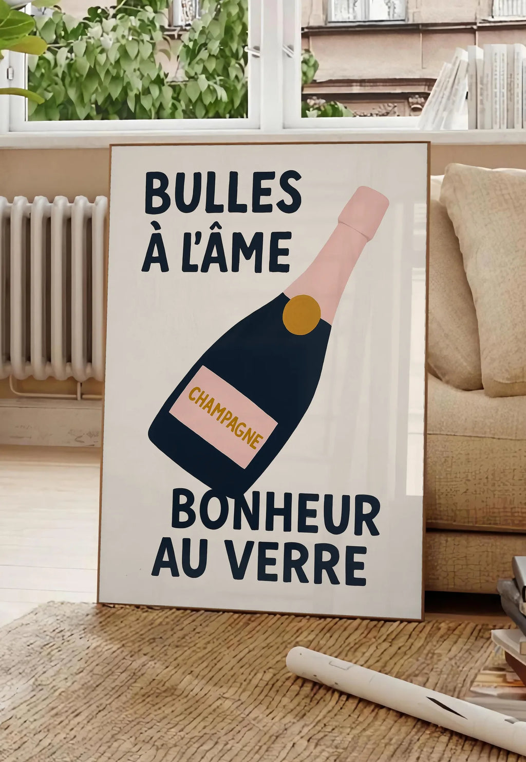 Poster affiche champagne Bulles a l'ame, posee au sol dans un salon parisien, devant une grande fenetre donnant sur un immeuble haussmannien, entre un ficus et un canape creme