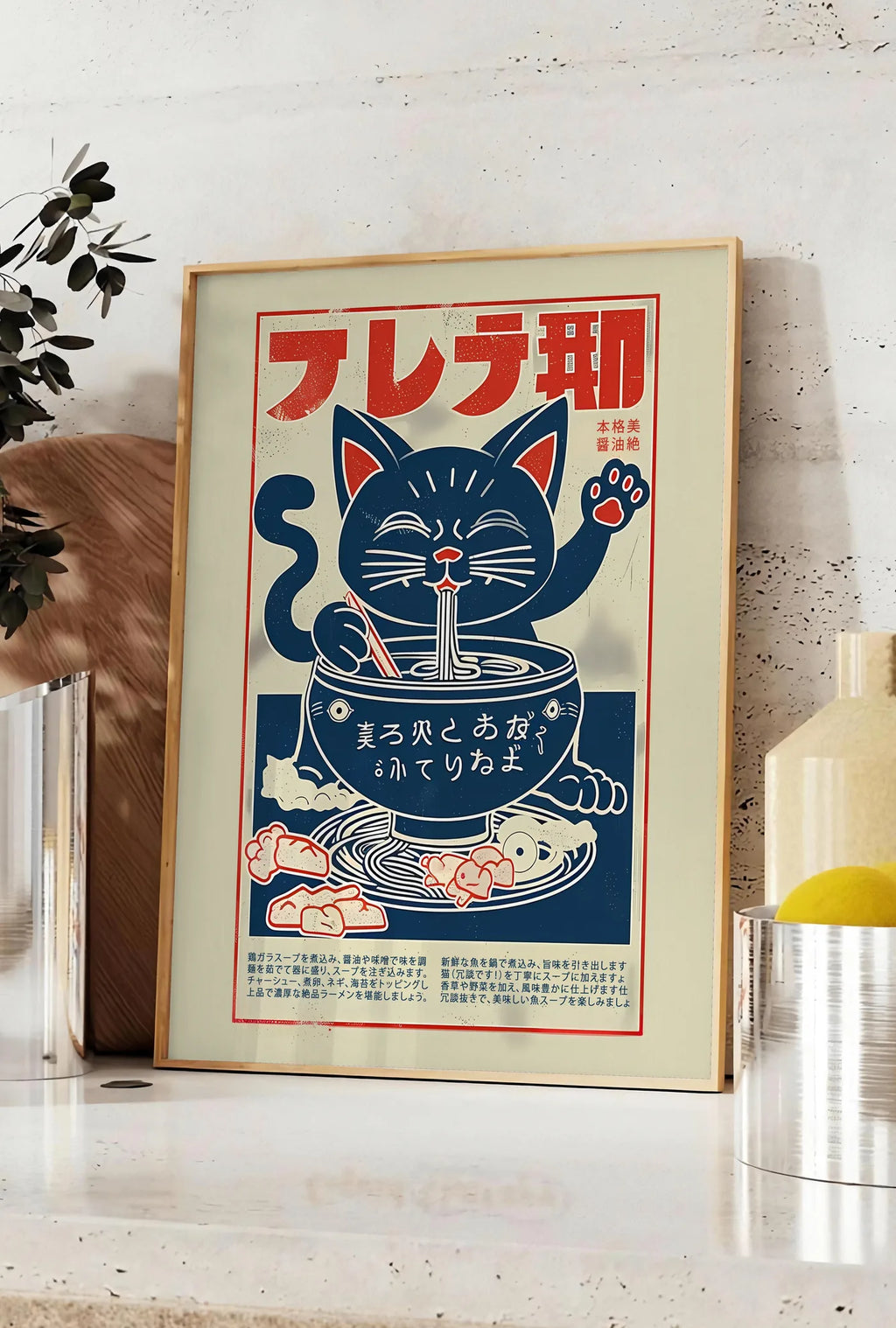 Affiche affiche chat ramen enseigne, posee sur un plan de travail de cuisine en pierre claire, entre une branche d'eucalyptus en vase et un bocal de citrons