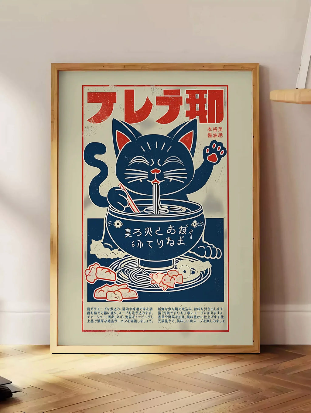 Estampe affiche chat ramen enseigne, posee au sol dans un coin salon, sur un parquet a chevrons, pres d'une table d'appoint en chene chargee de livres