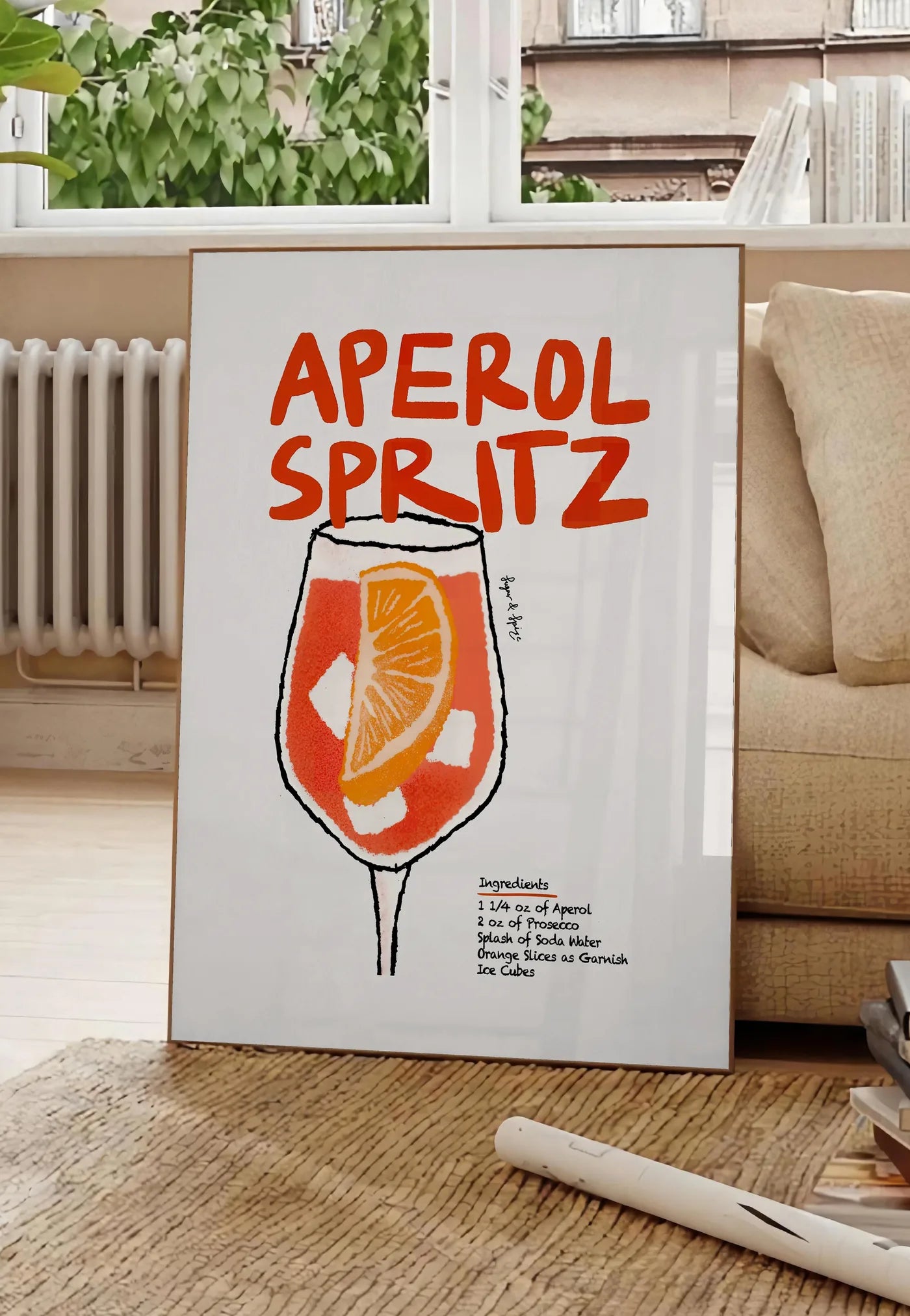 Poster verre d'Aperol Spritz, posee au sol dans un salon parisien, devant une grande fenetre donnant sur un immeuble haussmannien, entre un ficus et un canape creme