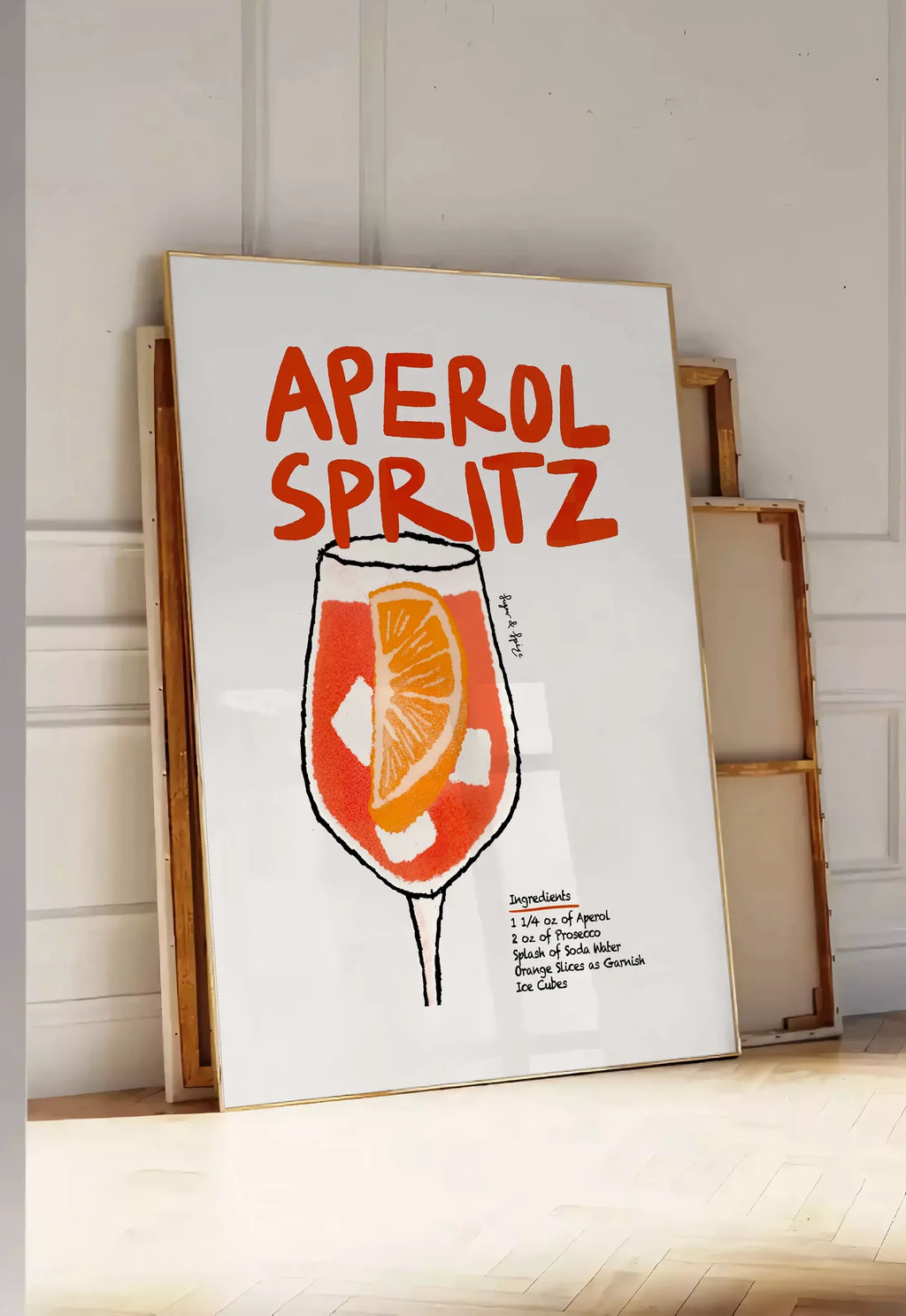 Tirage encadrable verre d'Aperol Spritz, posee au sol dans une entree lumineuse, contre un mur a panneaux blancs, a cote de chassis en bois empiles
