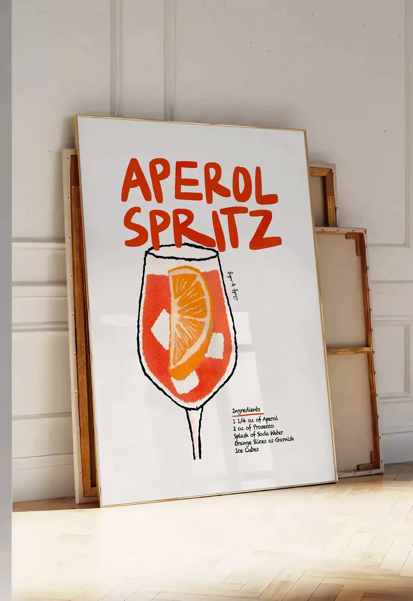 Tirage encadrable verre d'Aperol Spritz, posee au sol dans une entree lumineuse, contre un mur a panneaux blancs, a cote de chassis en bois empiles