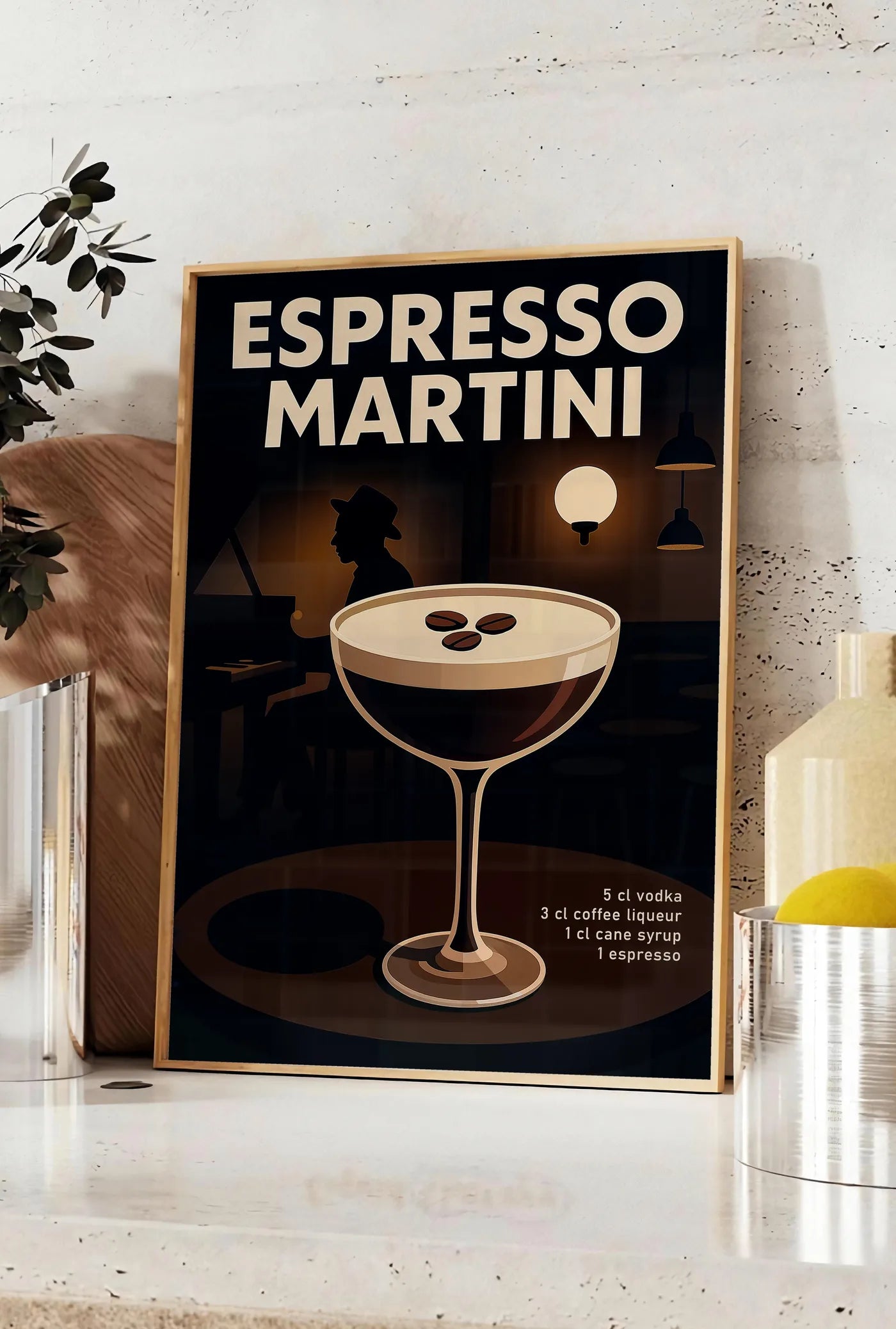 Affiche affiche Espresso Martini, posee sur un plan de travail de cuisine en pierre claire, entre une branche d'eucalyptus en vase et un bocal de citrons