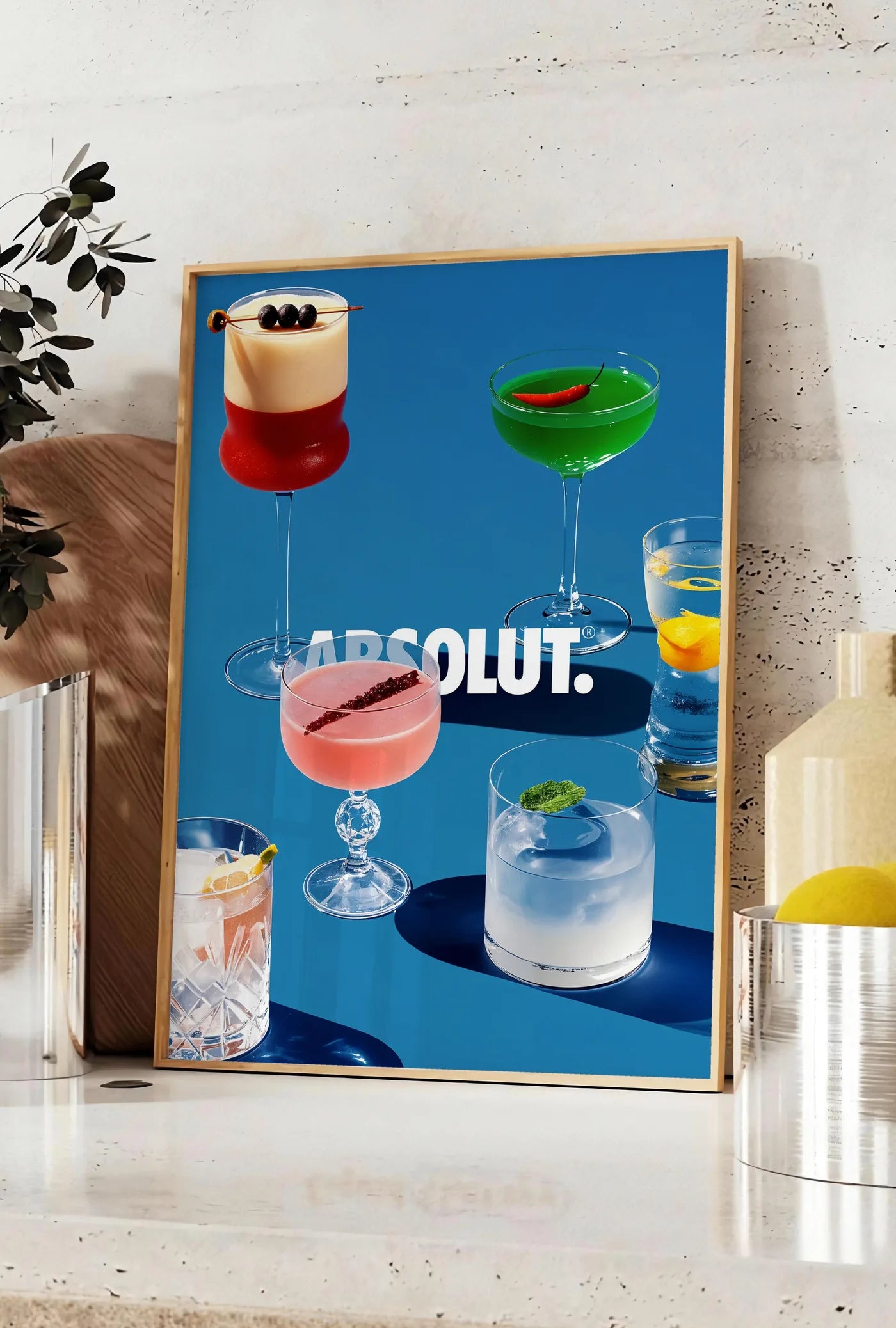 Affiche affiche cocktail collection, posee sur un plan de travail de cuisine en pierre claire, entre une branche d'eucalyptus en vase et un bocal de citrons