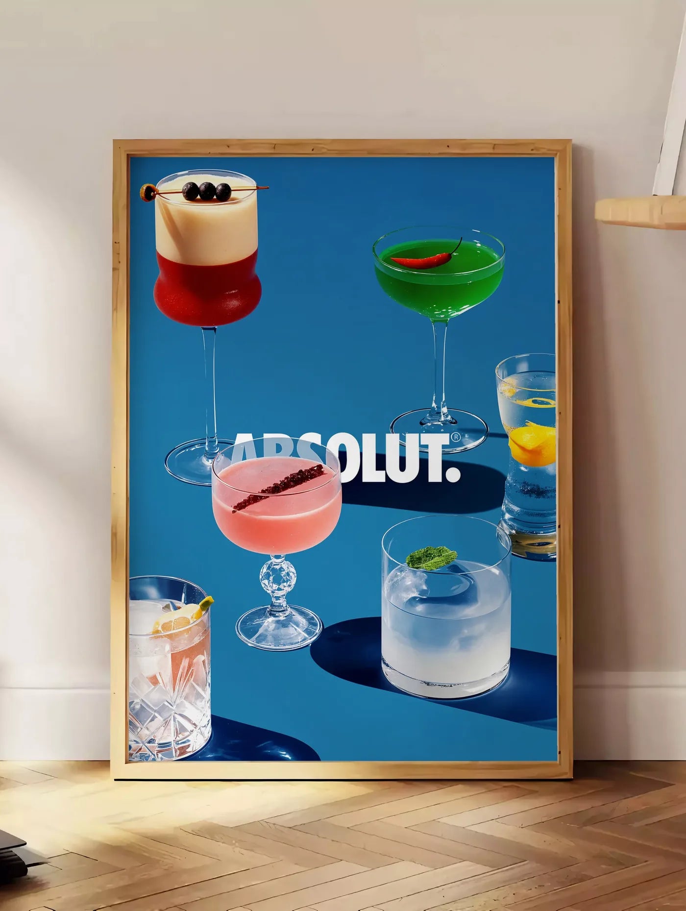 Estampe affiche cocktail collection, posee au sol dans un coin salon, sur un parquet a chevrons, pres d'une table d'appoint en chene chargee de livres