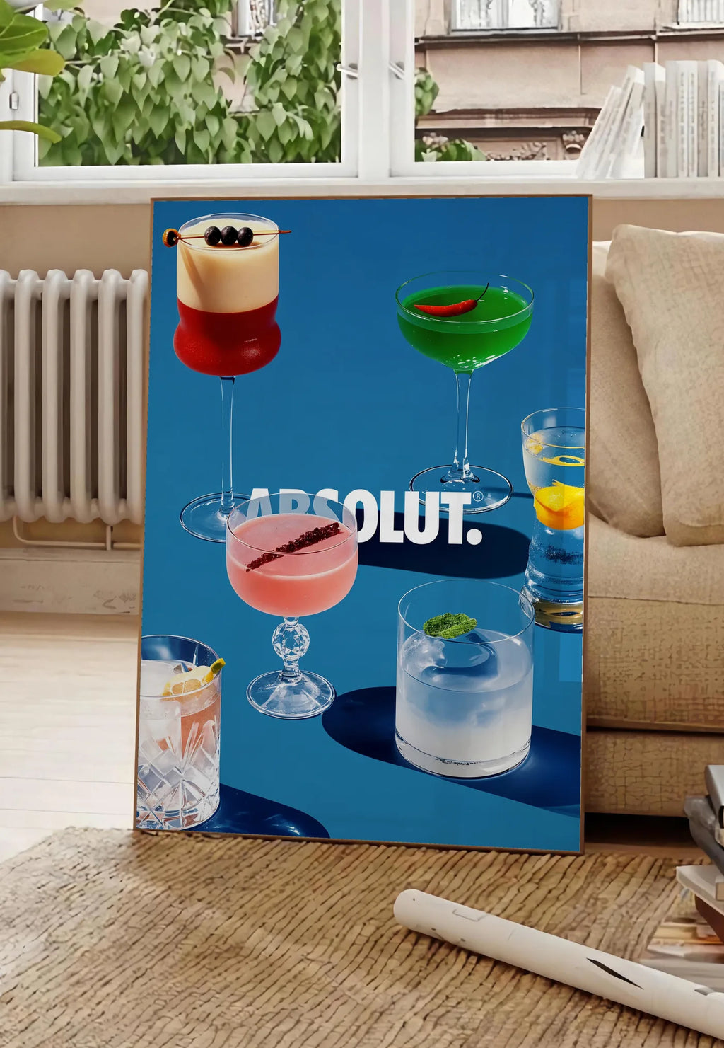 Poster affiche cocktail collection, posee au sol dans un salon parisien, devant une grande fenetre donnant sur un immeuble haussmannien, entre un ficus et un canape creme
