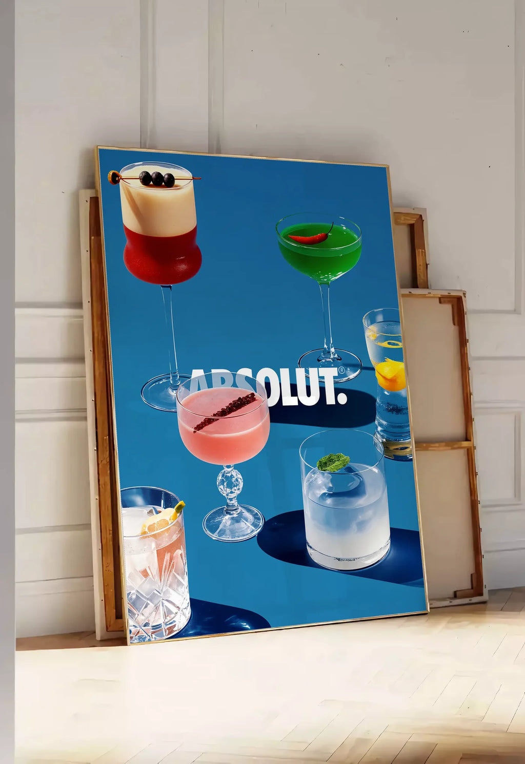 Tirage encadrable affiche cocktail collection, posee au sol dans une entree lumineuse, contre un mur a panneaux blancs, a cote de chassis en bois empiles