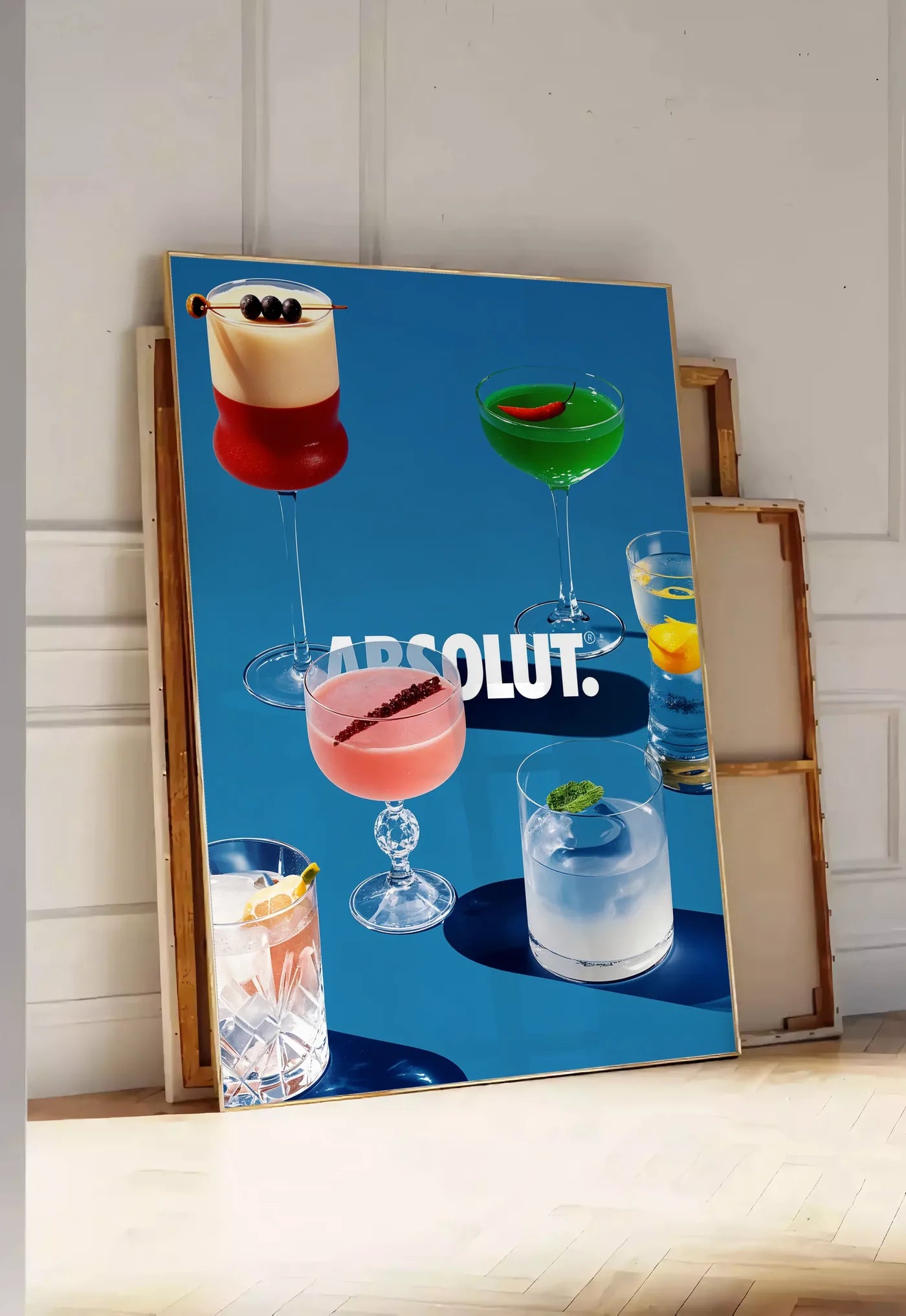 Tirage encadrable affiche cocktail collection, posee au sol dans une entree lumineuse, contre un mur a panneaux blancs, a cote de chassis en bois empiles