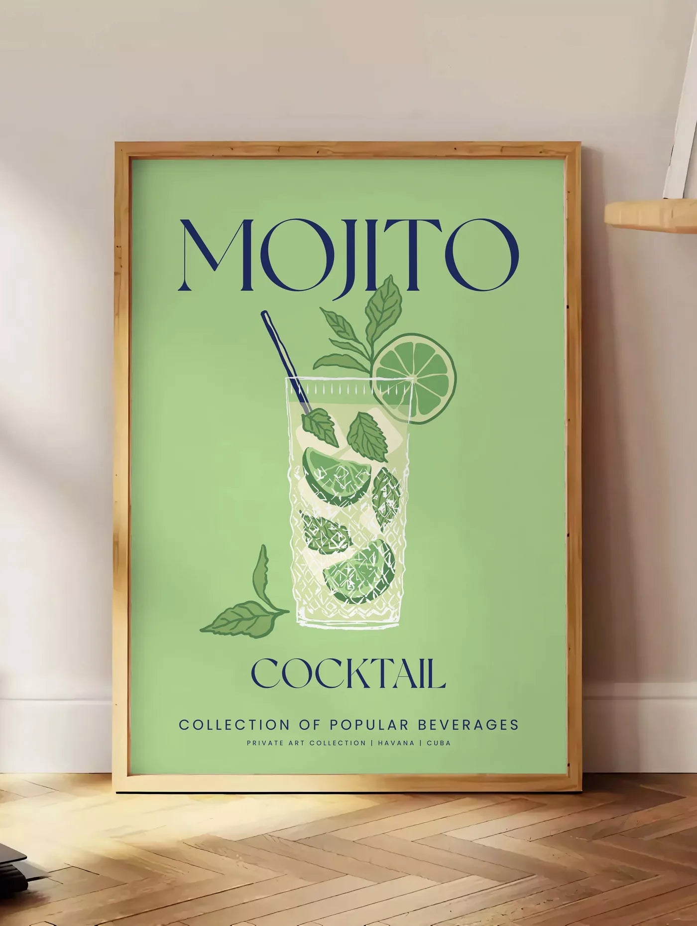 Estampe affiche mojito minimaliste, posee au sol dans un coin salon, sur un parquet a chevrons, pres d'une table d'appoint en chene chargee de livres