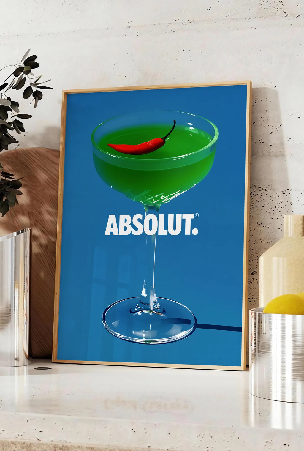Affiche affiche cocktail vert, posee sur un plan de travail de cuisine en pierre claire, entre une branche d'eucalyptus en vase et un bocal de citrons
